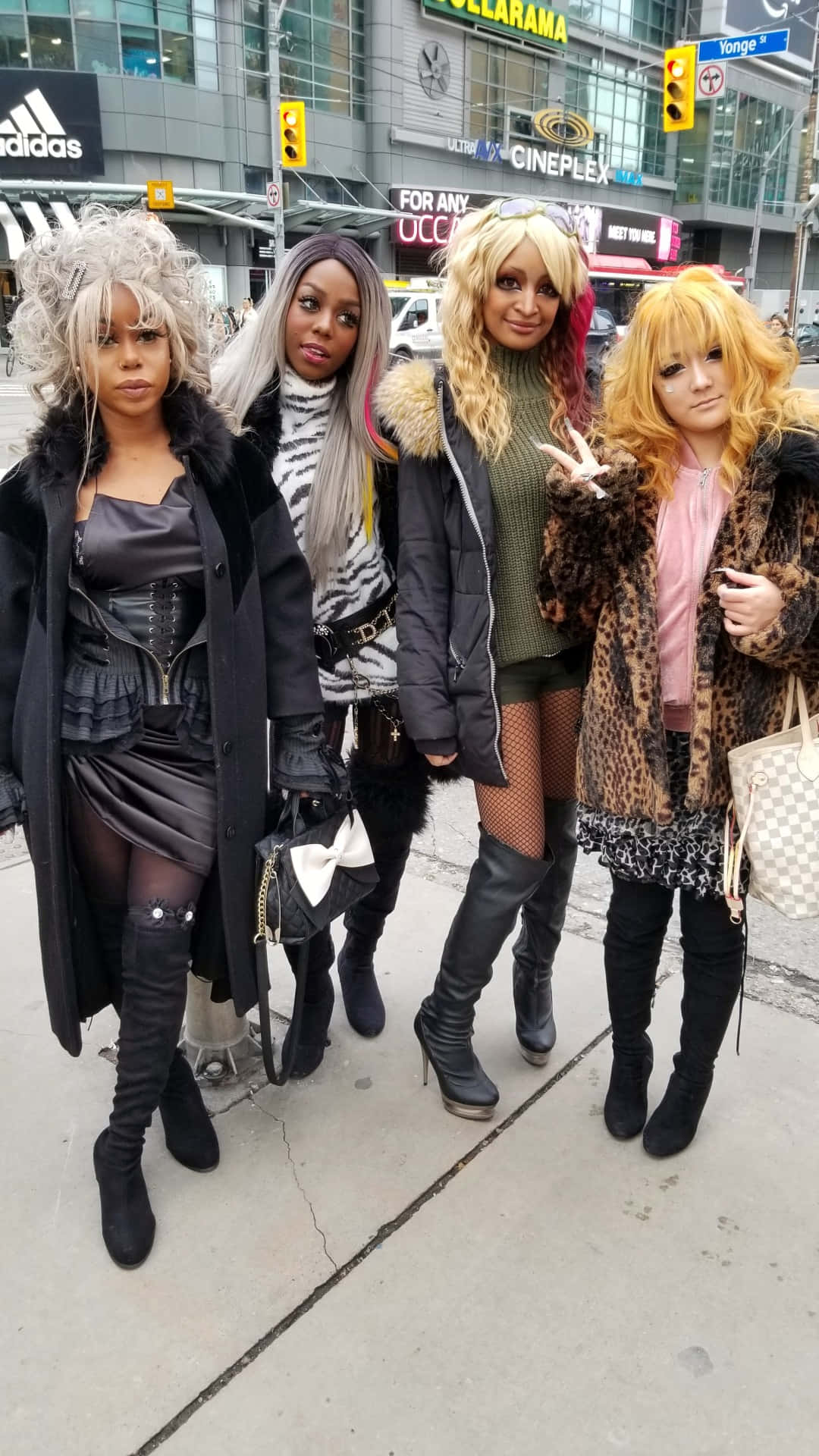 Gyaru Fashion 桌布 壁紙 — 四位身穿大膽角色扮演服裝的女性在商店櫥窗和交通燈附近的城市人行道上自信地擺姿勢。