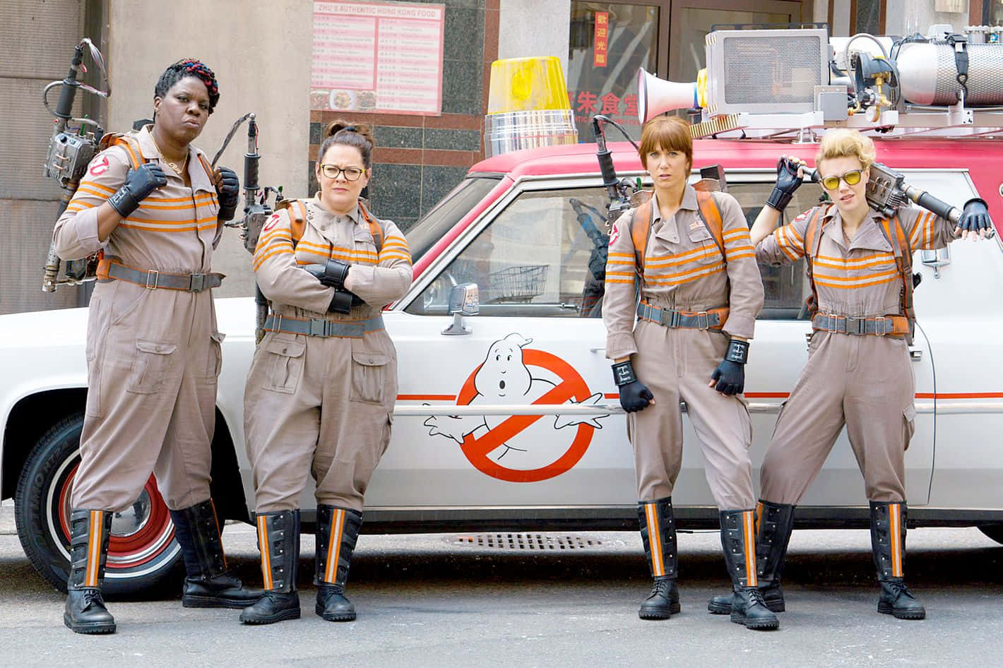 Ghostbusters 桌布 壁紙 — 四位身穿經典捉鬼敢死隊制服嘅女士，自信地企喺佢哋配備質子背包嘅貨車旁邊嘅城市街道上。