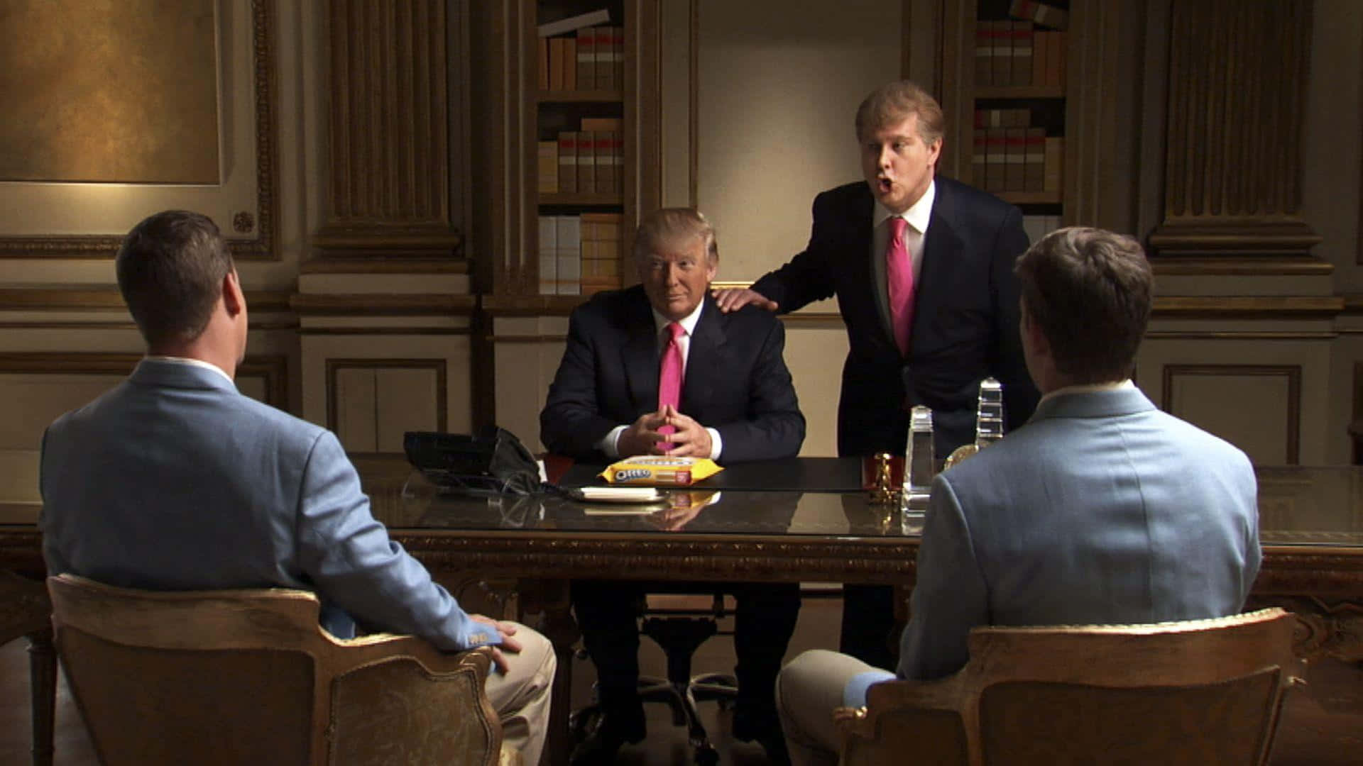 trump 桌布 壁紙 — 四位身穿西裝的男士坐在或站在一張拋光木桌旁，身處一個有書架和華麗牆壁的正式辦公室。