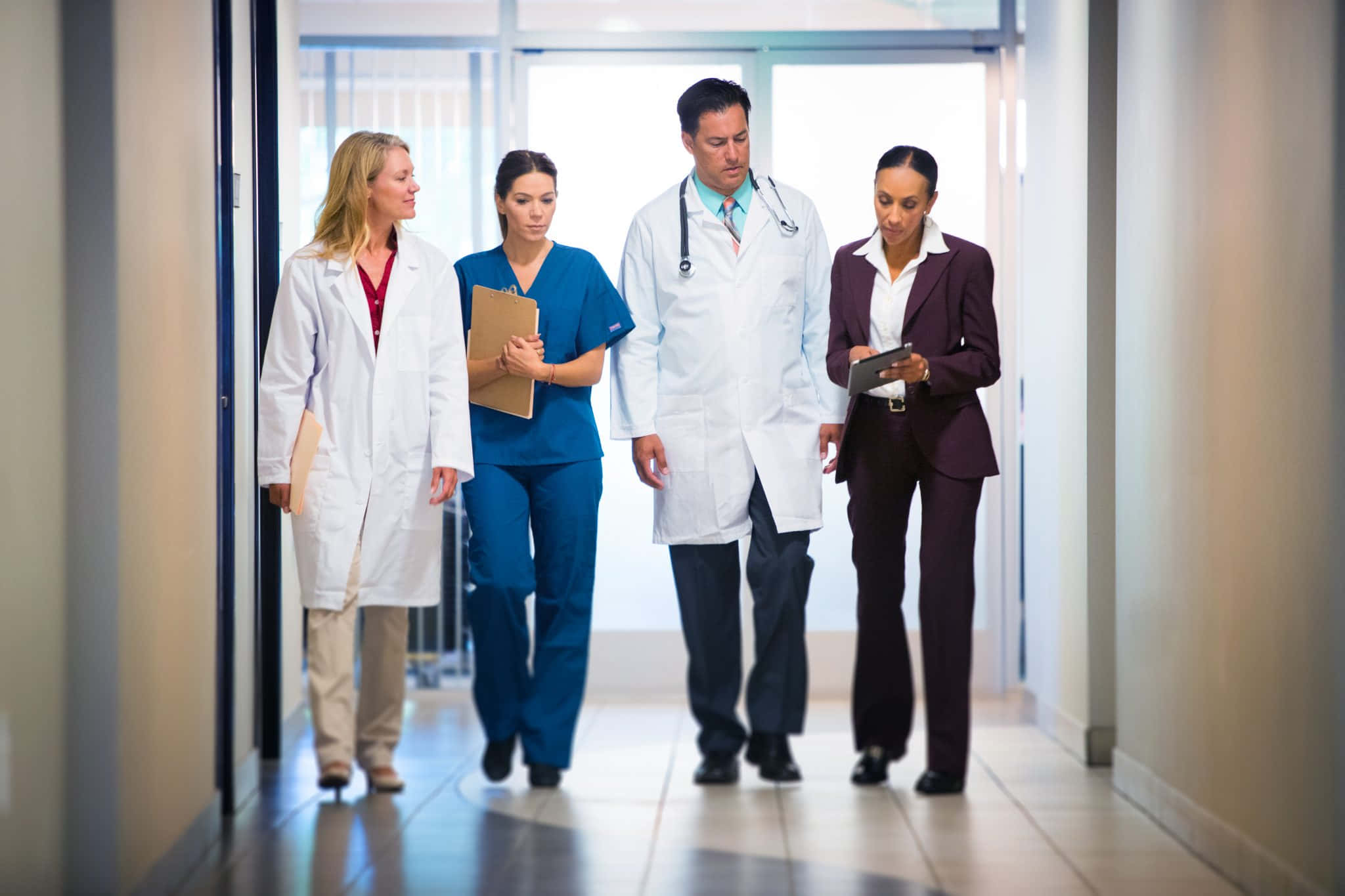 Nursing 桌布 壁紙 — 四位醫療專業人士在明亮的醫院走廊上行走，專注於病人護理和協作。