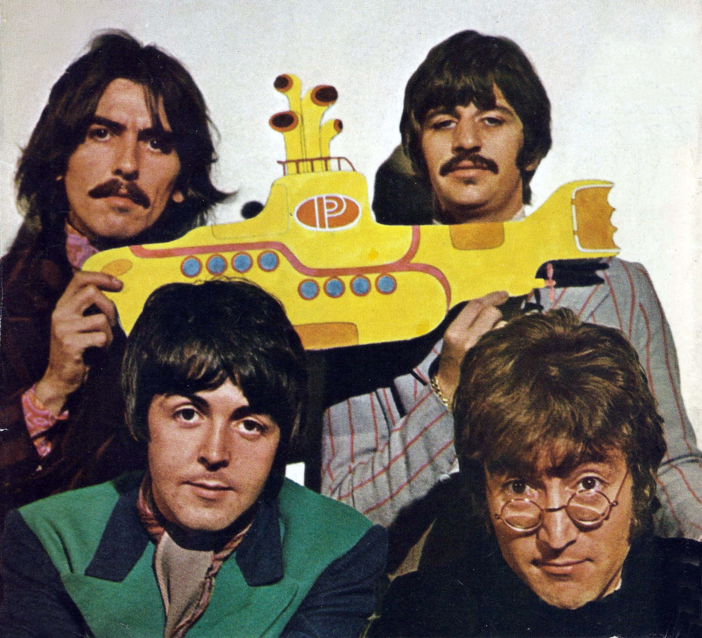 Yellow Submarine 桌布 壁紙 — 四位長髮男士在純色背景前拿著一個大型黃色潛水艇剪紙。