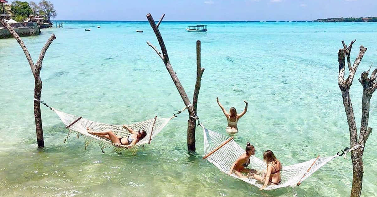 Bali Island 桌布 壁紙 — 四個人在懸掛在水晶般清澈的碧綠海水上的吊床上放鬆，遠處可見一艘船。