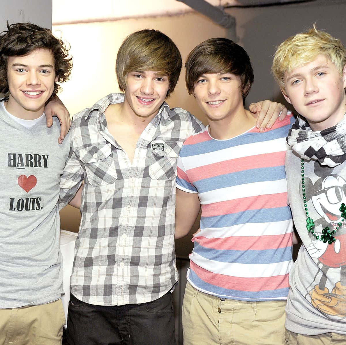 One Direction 桌布 壁紙 — 四個年輕男子互相搭著膊頭，穿著休閒服裝，在純色背景前燦爛微笑。