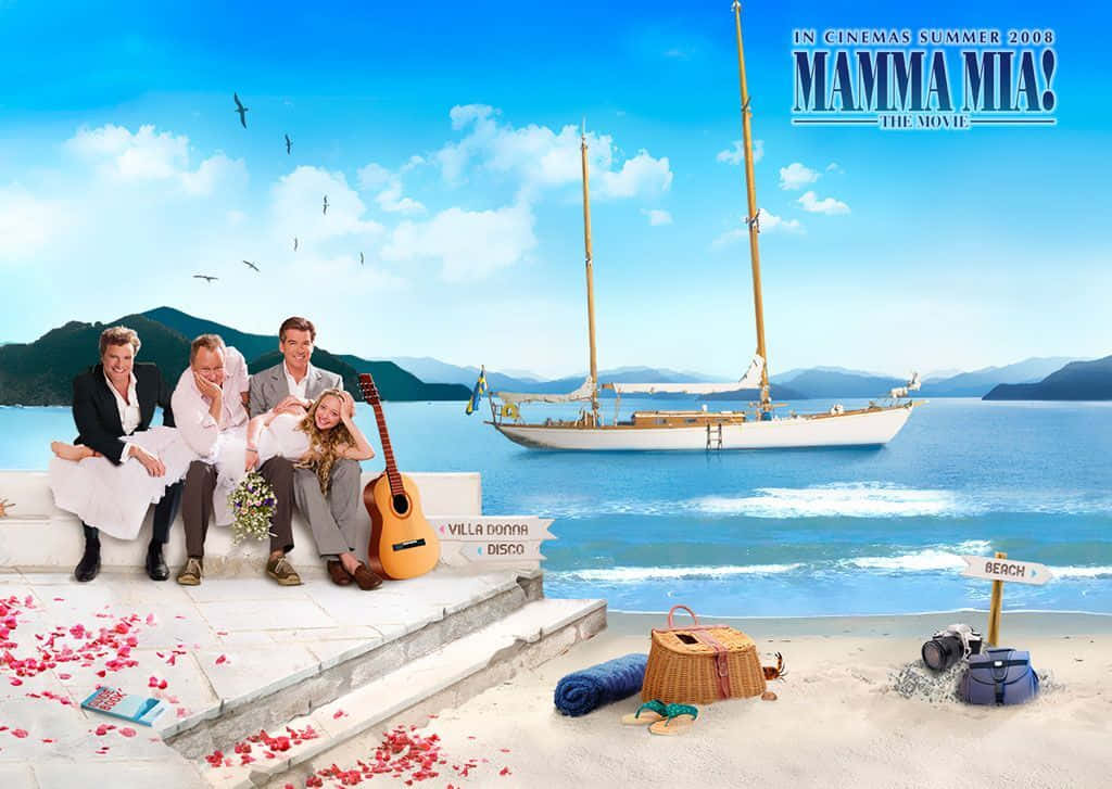 Mamma Mia 桌布 壁紙 — 四個快樂的人坐在海邊的石頭邊緣，旁邊有一把結他和散落的玫瑰花瓣，一艘帆船在明亮的藍天下滑過碧綠的海水。