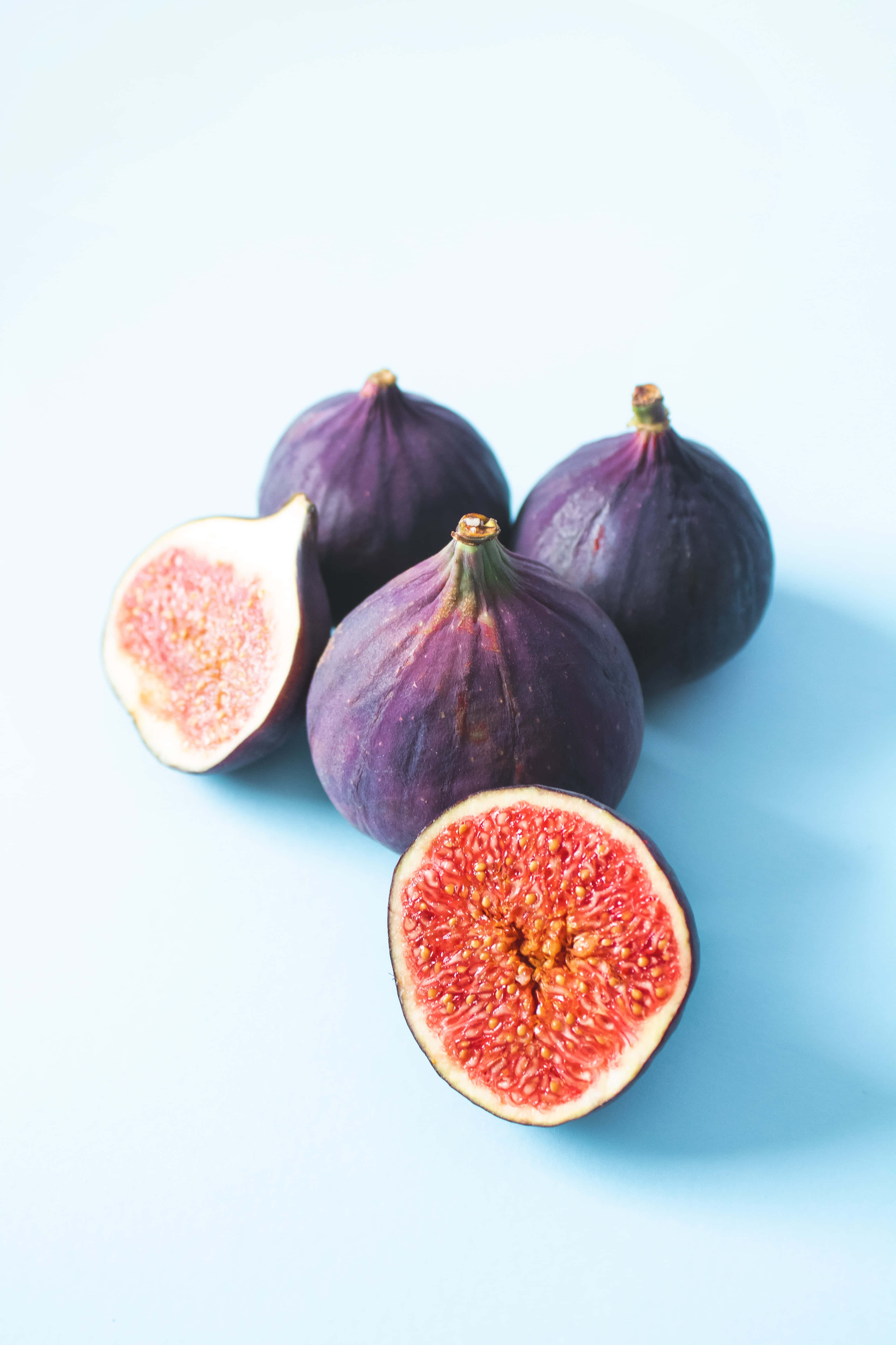 Purple Figs 桌布 壁紙 — 四個成熟的紫色無花果，帶有 juicy 粉紅色內部，放在柔軟的藍色背景上。