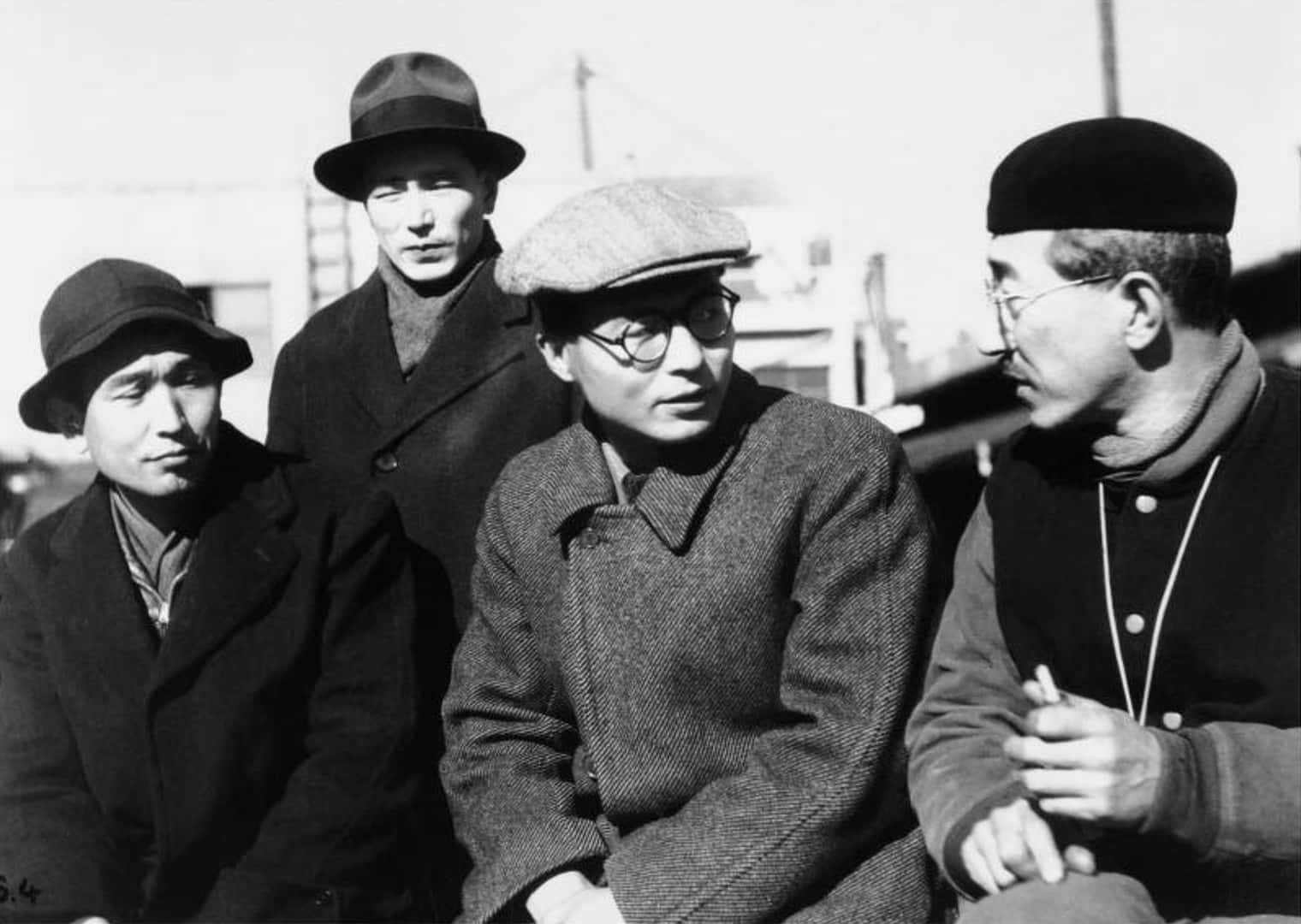 Akira Kurosawa 桌布 壁紙 — 四個戴帽穿外套的男人，表情嚴肅地坐在一起，是一張自然隨拍的黑白街頭照片。