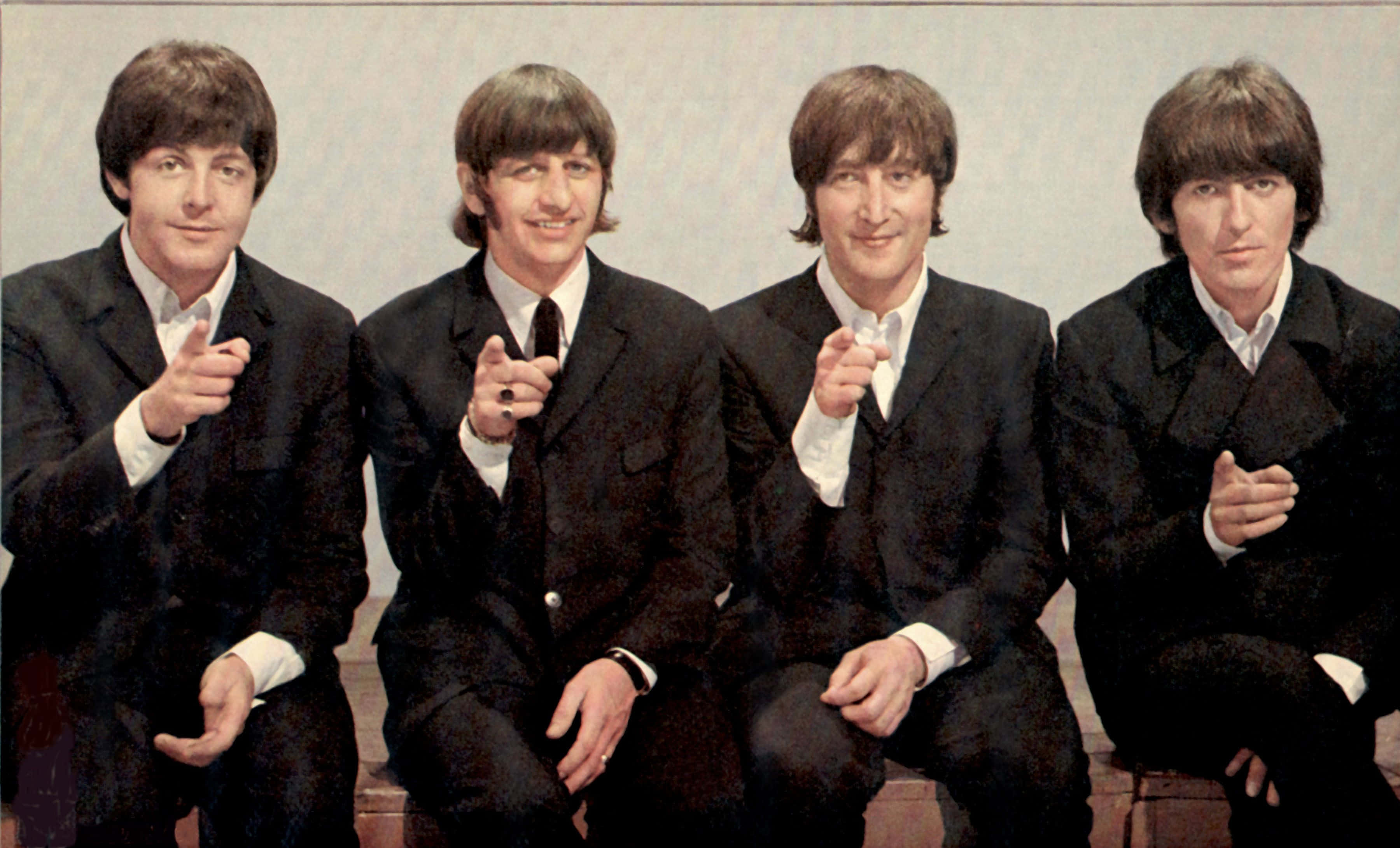 the beatles 桌布 壁紙 — 四個穿著黑色西裝的男人並排坐著，自信地微笑著指向相機。