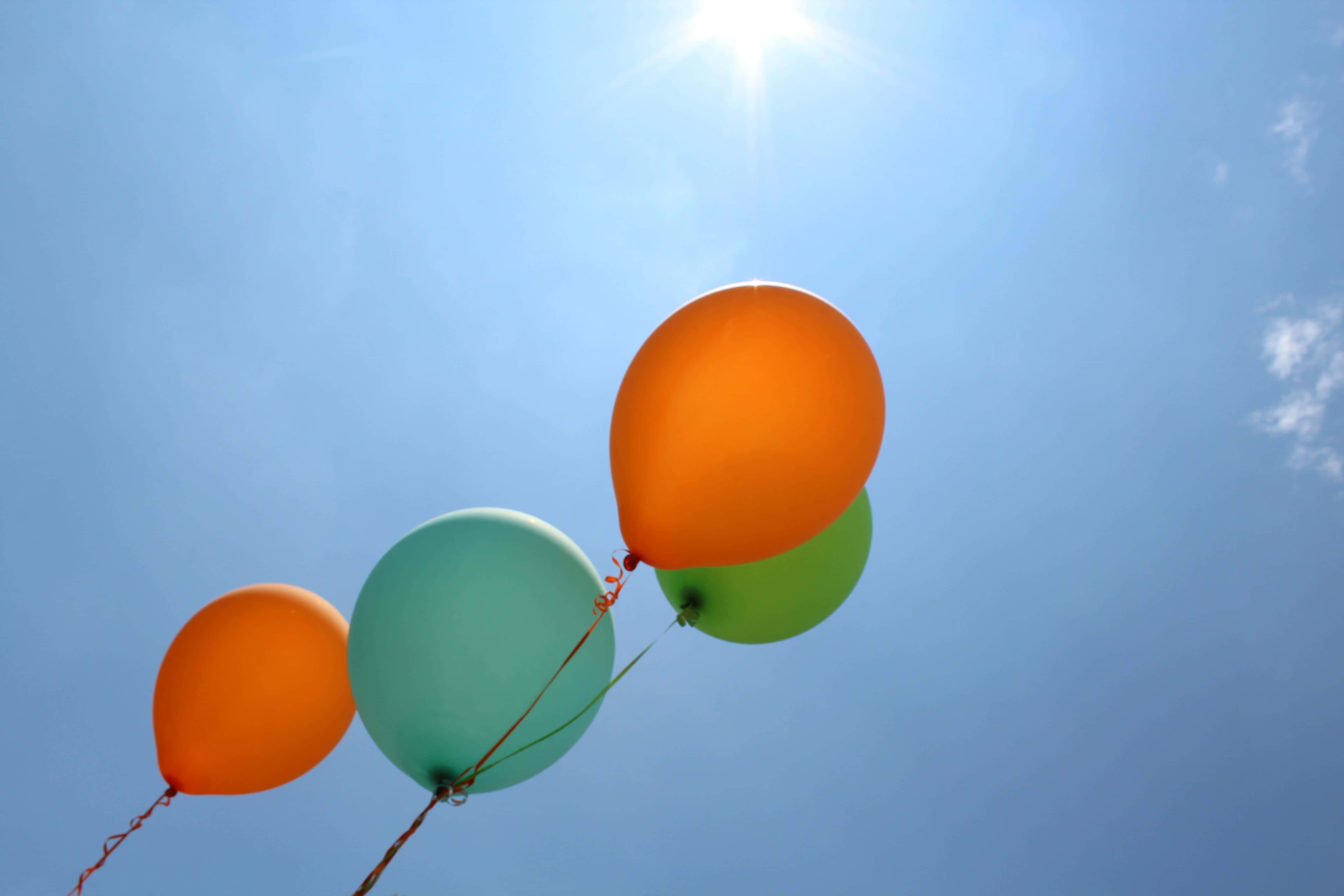 Balloon 桌布 壁紙 — 四個色彩繽紛的氣球在明亮的藍天和陽光照耀下向上飄浮。