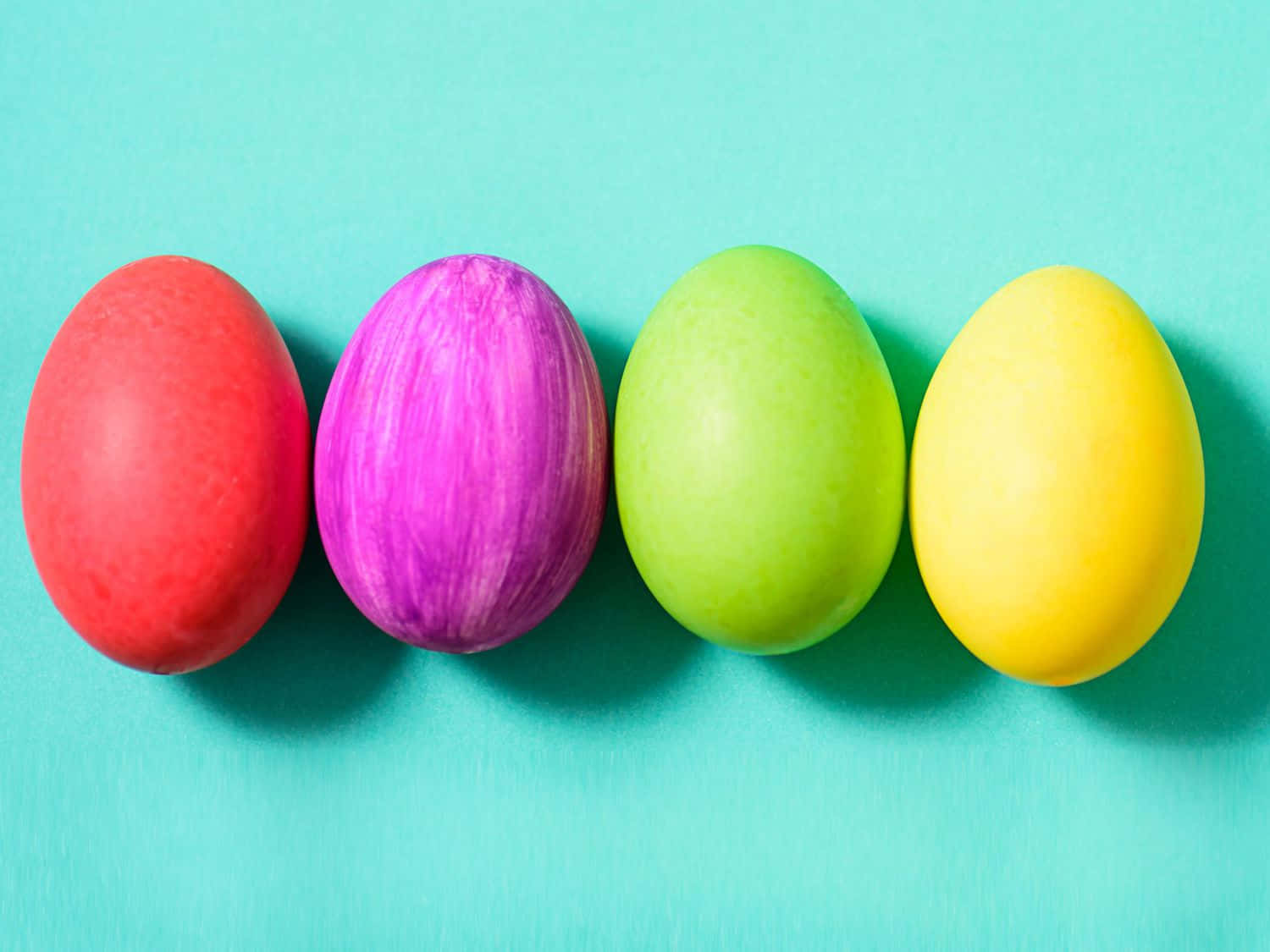 Eggs 桌布 壁紙 — 四個色彩鮮豔的復活節蛋（紅色、紫色、綠色和黃色）整齊地排列在青綠色背景上。