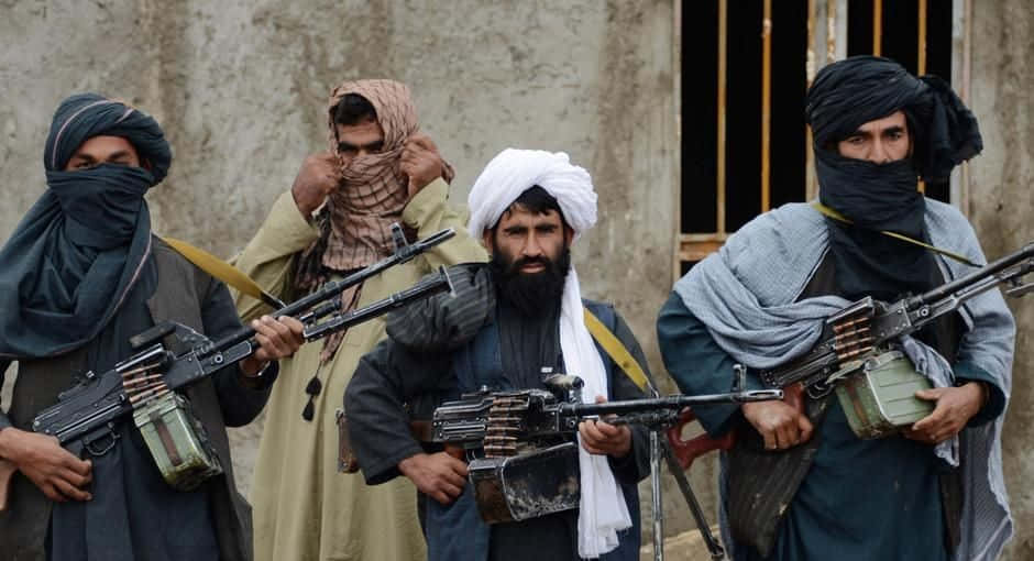 Taliban 桌布 壁紙 — 四名戴頭巾和頭飾的武裝男子站在骯髒的城市小巷中，手持重型機槍。