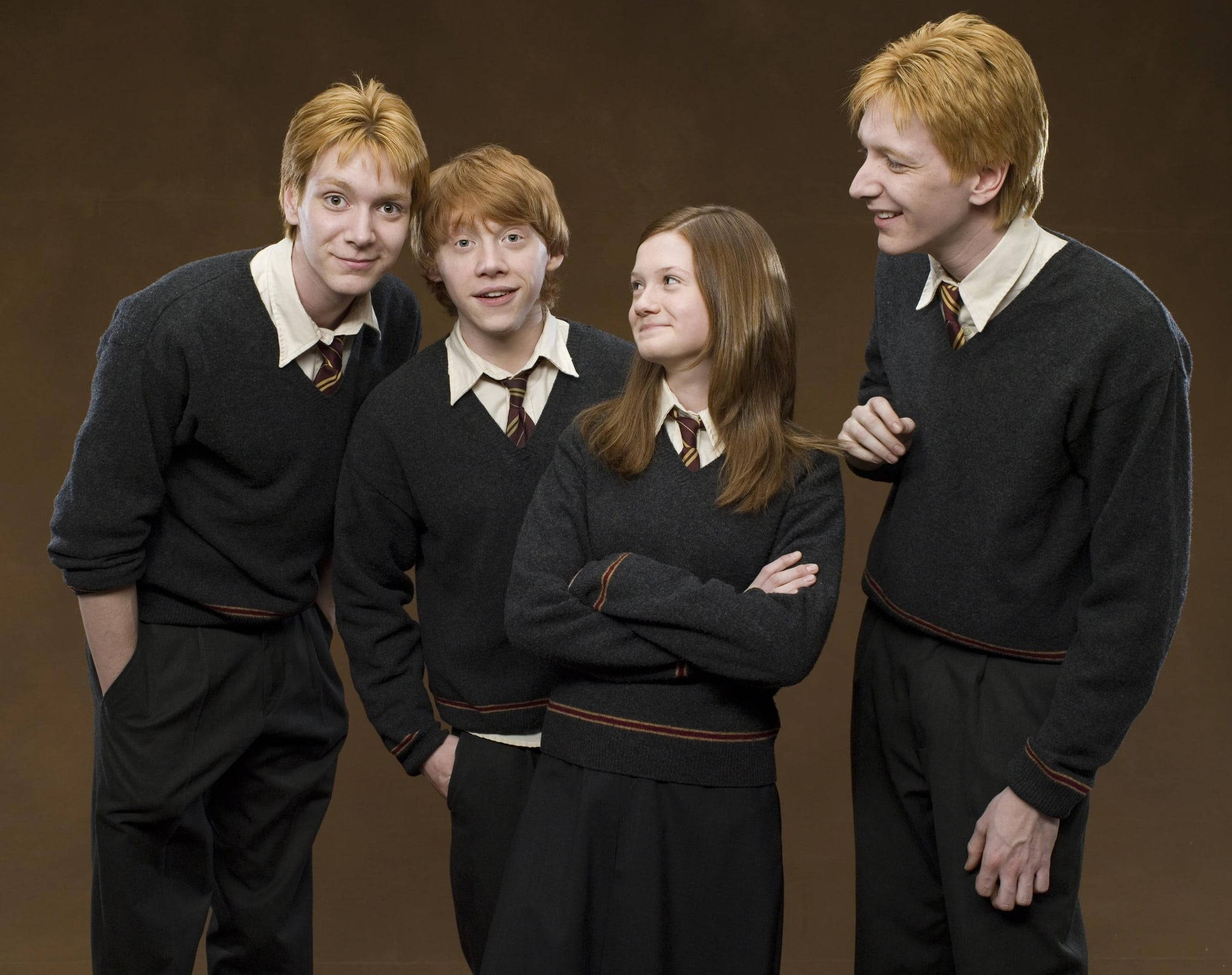 Ron Weasley 桌布 壁紙 — 四名穿著霍格華茲制服的學生在溫暖燈光下，於純棕色攝影棚背景前一起擺姿勢。