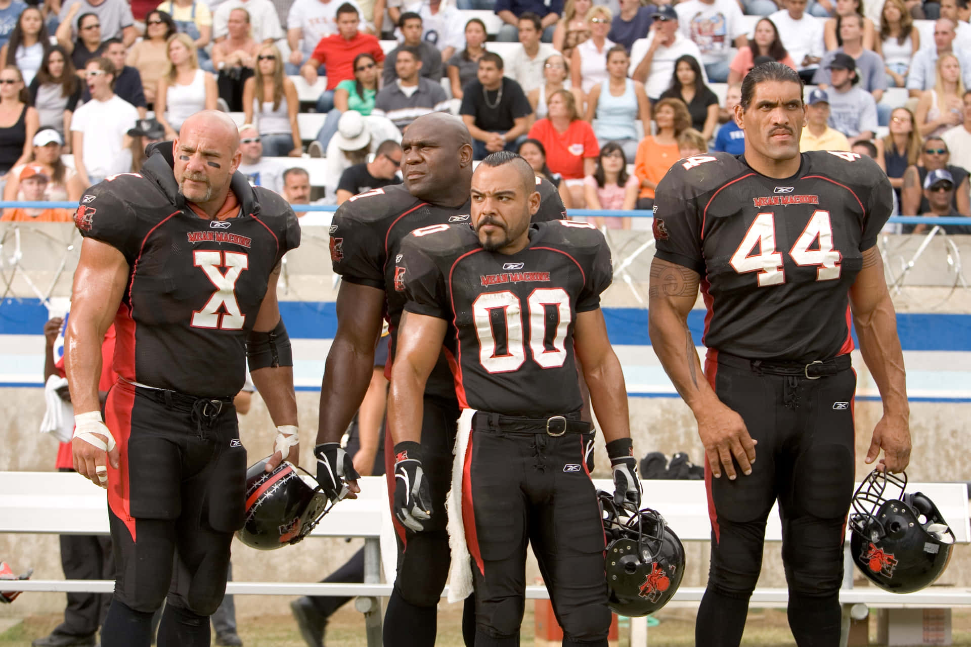 《The Longest Yard》Bob Sapp 壁紙 — 四名身穿黑紅球衣的激烈足球員莊嚴地站在球場上，身後有觀眾觀看。