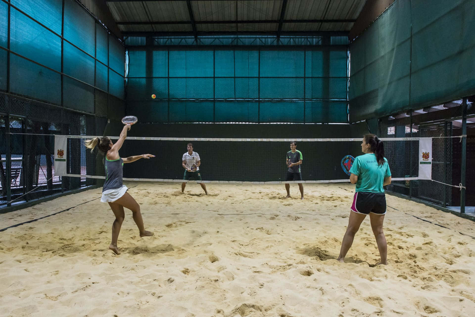 Beach Tennis 桌布 壁紙 — 四名選手在青綠色室內場地屋頂下激烈地進行沙灘排球比賽。