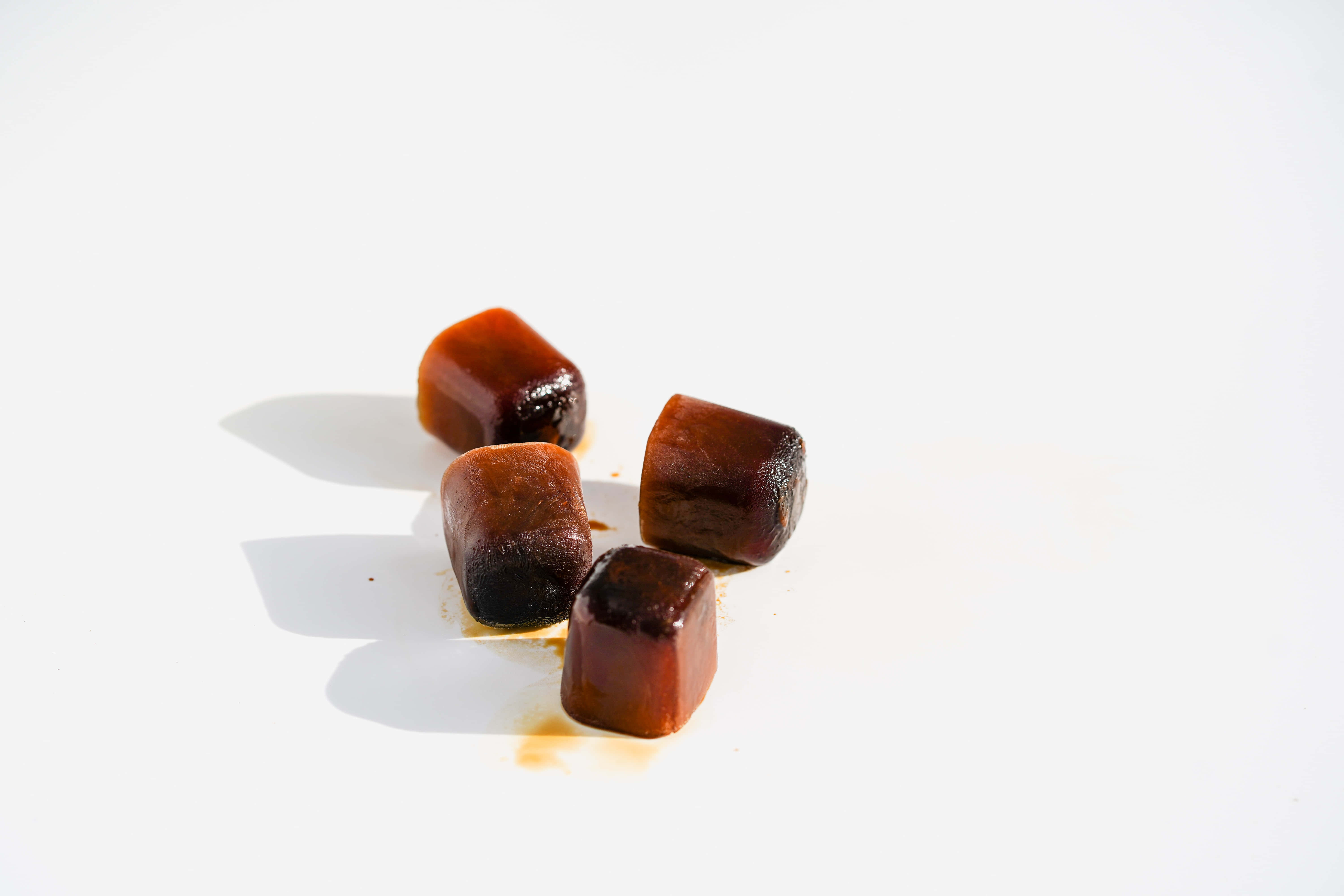 Caramel 桌布 壁紙 — 四塊光澤的咖啡冰塊在明亮的白色表面上微微融化，投下柔和的陰影。