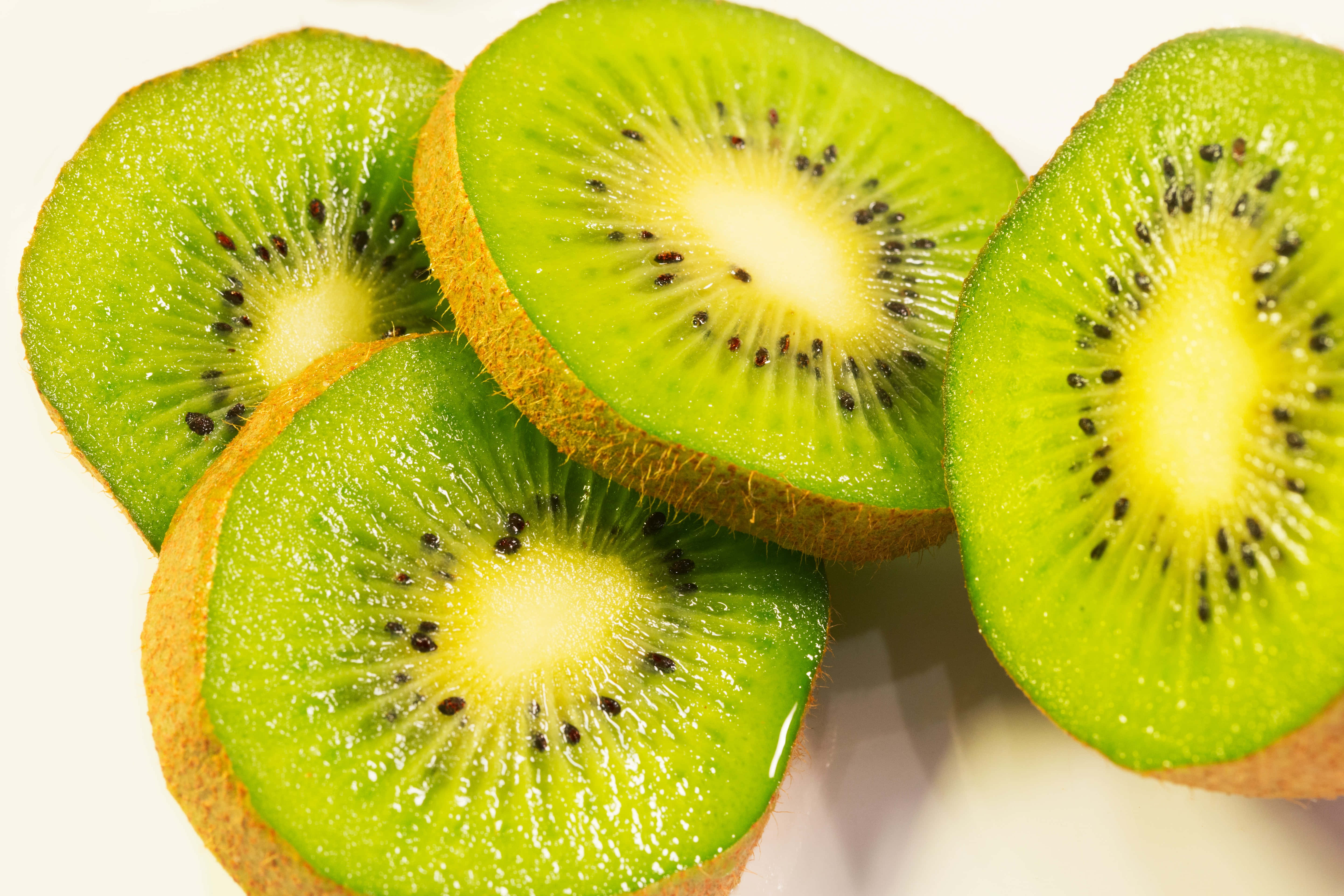Kiwi 桌布 壁紙 — 四塊鮮綠色奇異果切片排列成一簇，在明亮的白色背景上顯露出多汁的果肉和黑色種子。