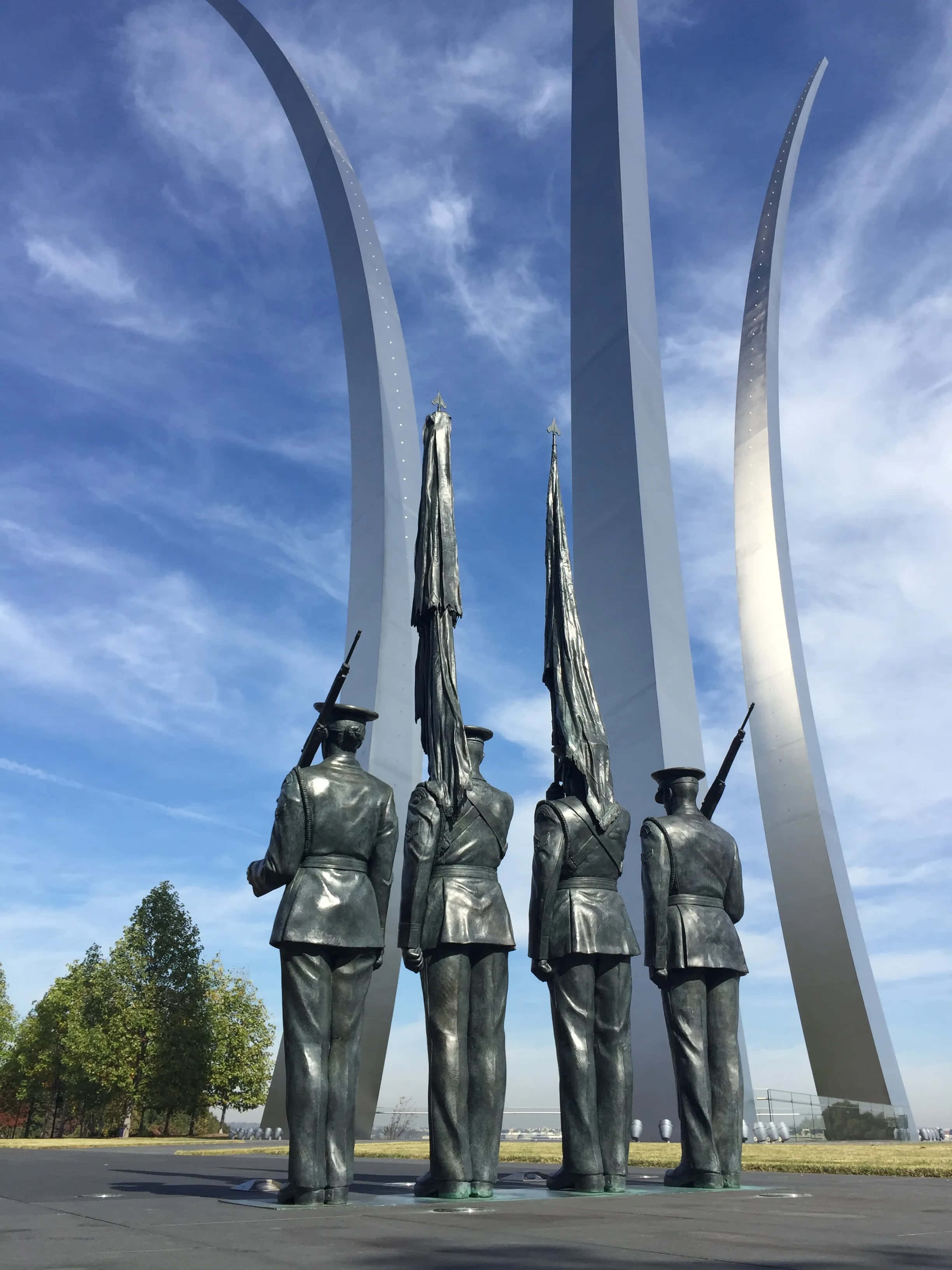 Memorial 桌布 壁紙 — 四尊青銅士兵雕像持步槍和旗幟立正，矗立在宏偉的銀色拱門下，背景是明亮的藍天。