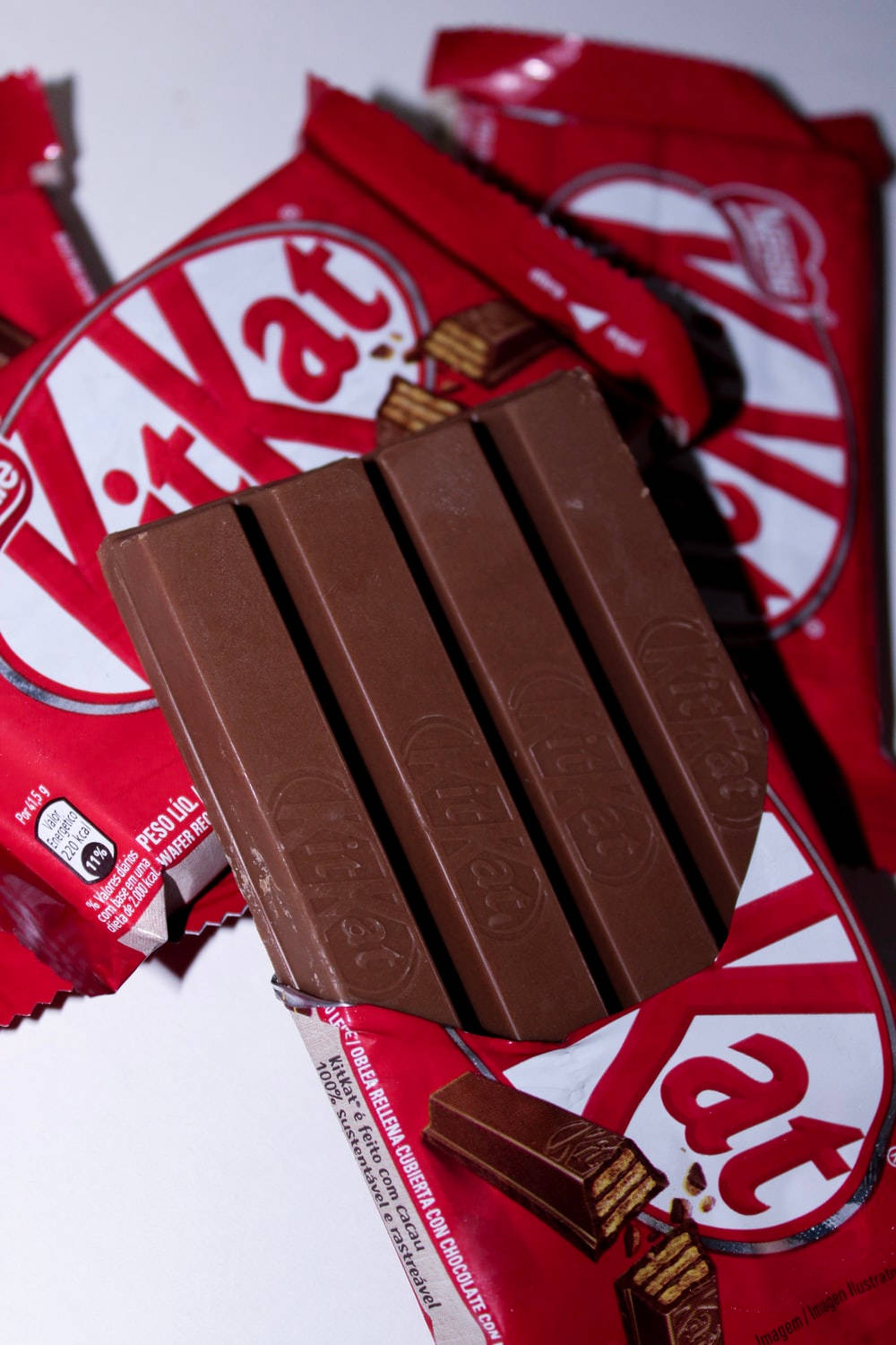 四指 Kit Kat 巧克力已解開包裝 壁紙 — 一個KitKat朱古力棒的特寫，放在紅色KitKat包裝紙上，細節清晰，棕色色調豐富。