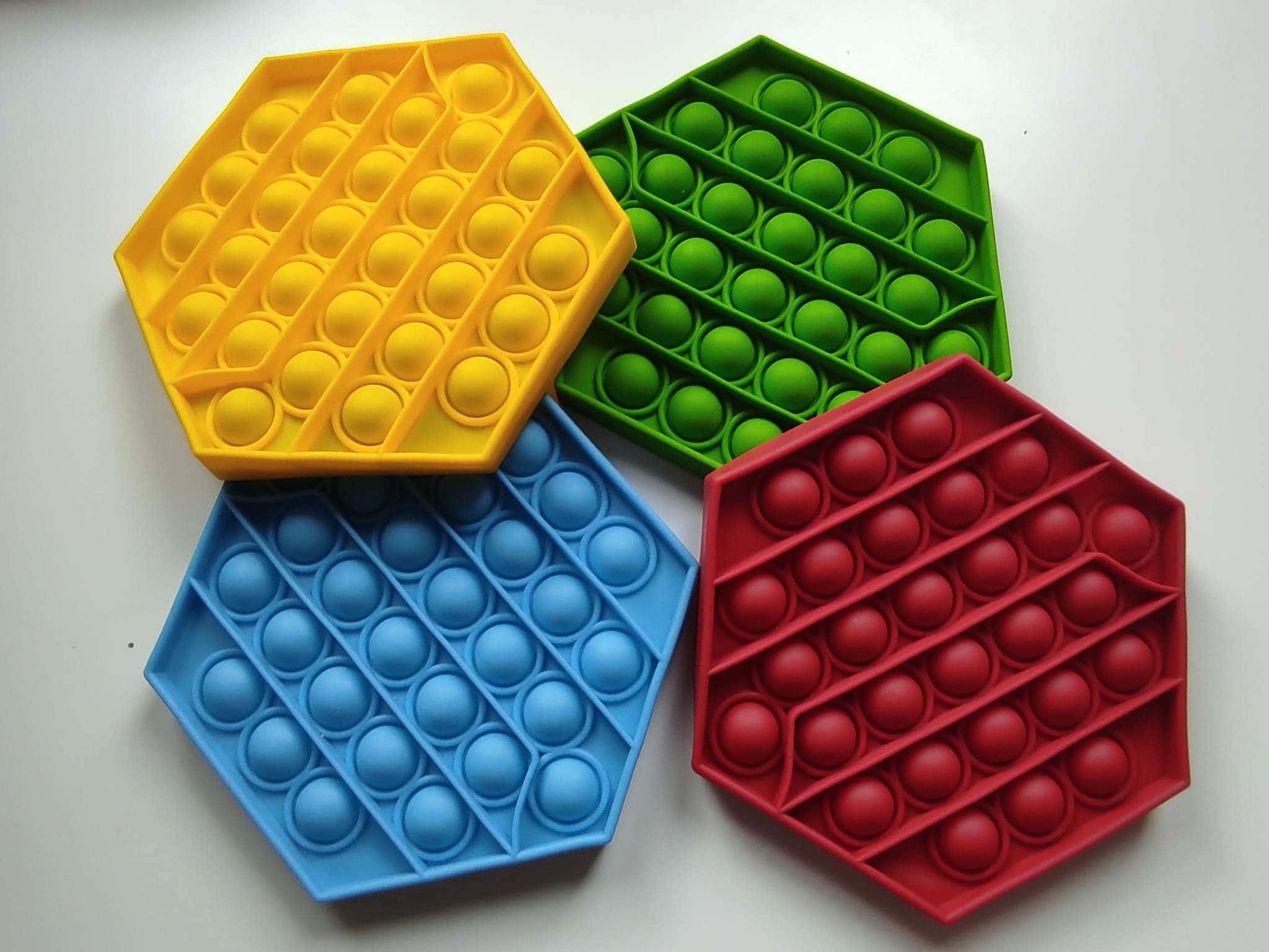 四款八角形Pop It玩具圖 壁紙 — 四個色彩繽紛的六角形彈出式減壓玩具，分別為黃色、綠色、藍色和紅色，排列在純白色表面上。