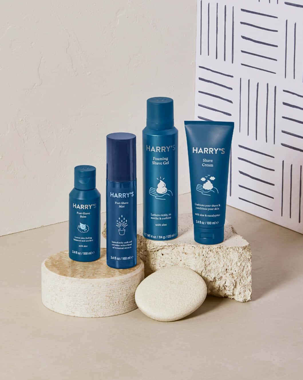 Shaving Cream 桌布 壁紙 — 四款藍色Harry's美容產品排列在質感石塊上，背景為極簡風格牆壁搭配幾何線條藝術。