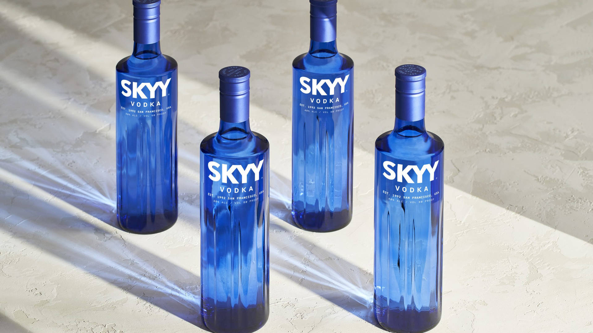四支藍色SKYY伏特加酒瓶在明亮的陽光下，置於紋理表面上。