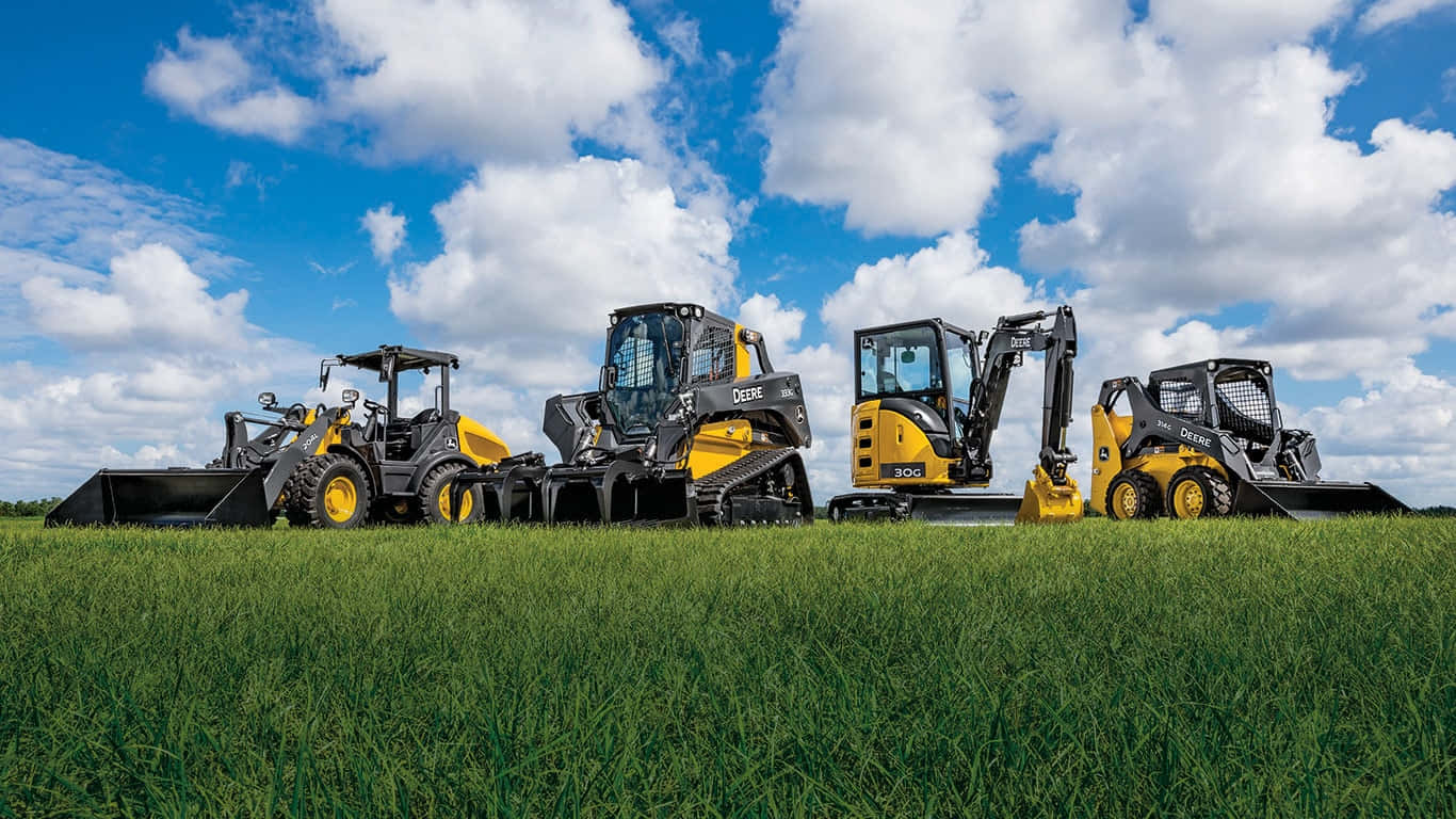 John Deere 桌布 壁紙 — 四部黃色John Deere建築機械排列在茂盛的綠色田野上，天空湛藍，白雲朵朵。