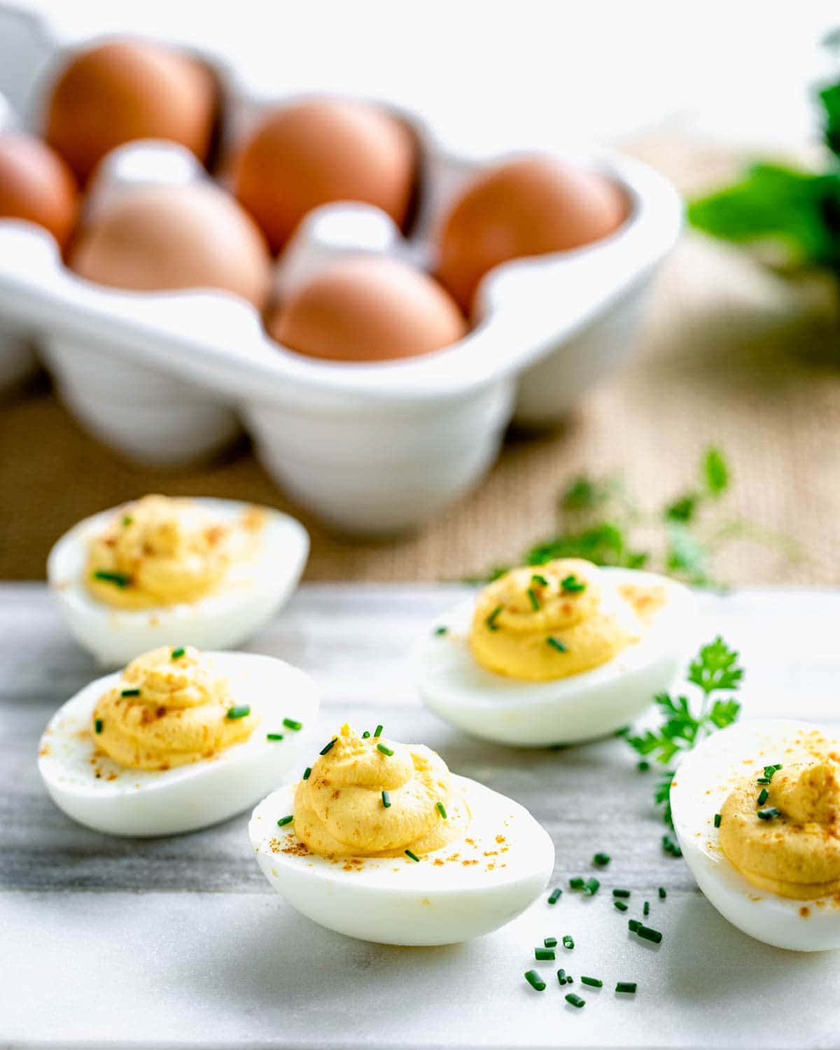 Eggs 桌布 壁紙 — 四隻魔鬼蛋飾以細香蔥，置於大理石面上，後方有一盒啡色雞蛋，呈現柔和焦點。