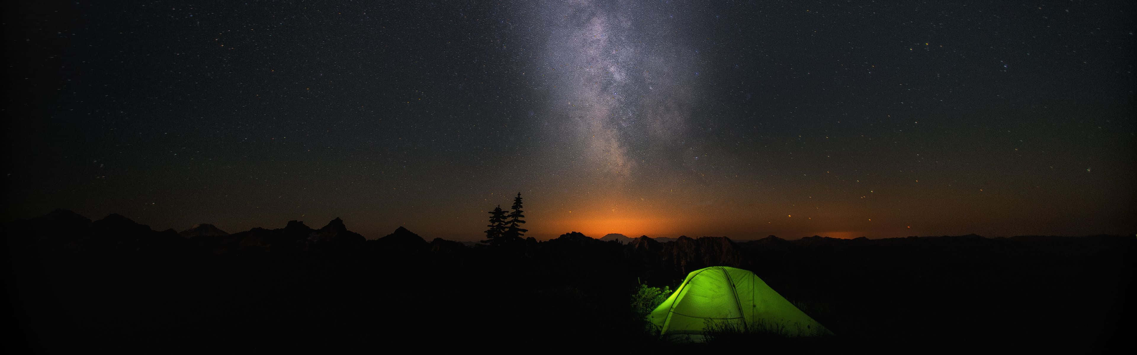在銀河拱起的星空下，黑暗山脈中的一個發光綠色帳篷。