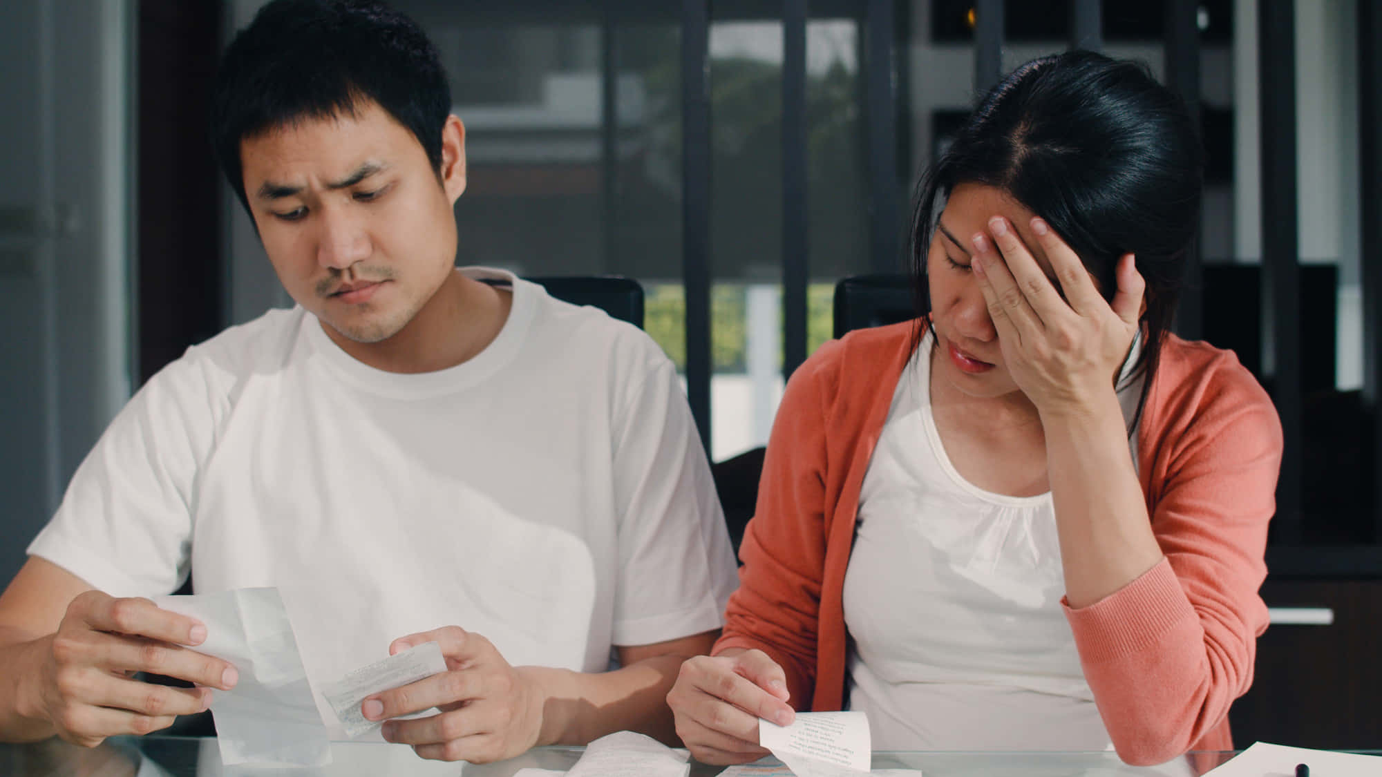 因帳單煩惱的年輕夫婦 壁紙 — 一對壓力大的夫婦坐在桌旁，帶著憂慮的表情查看帳單，其中一名女子因沮喪而抱頭。