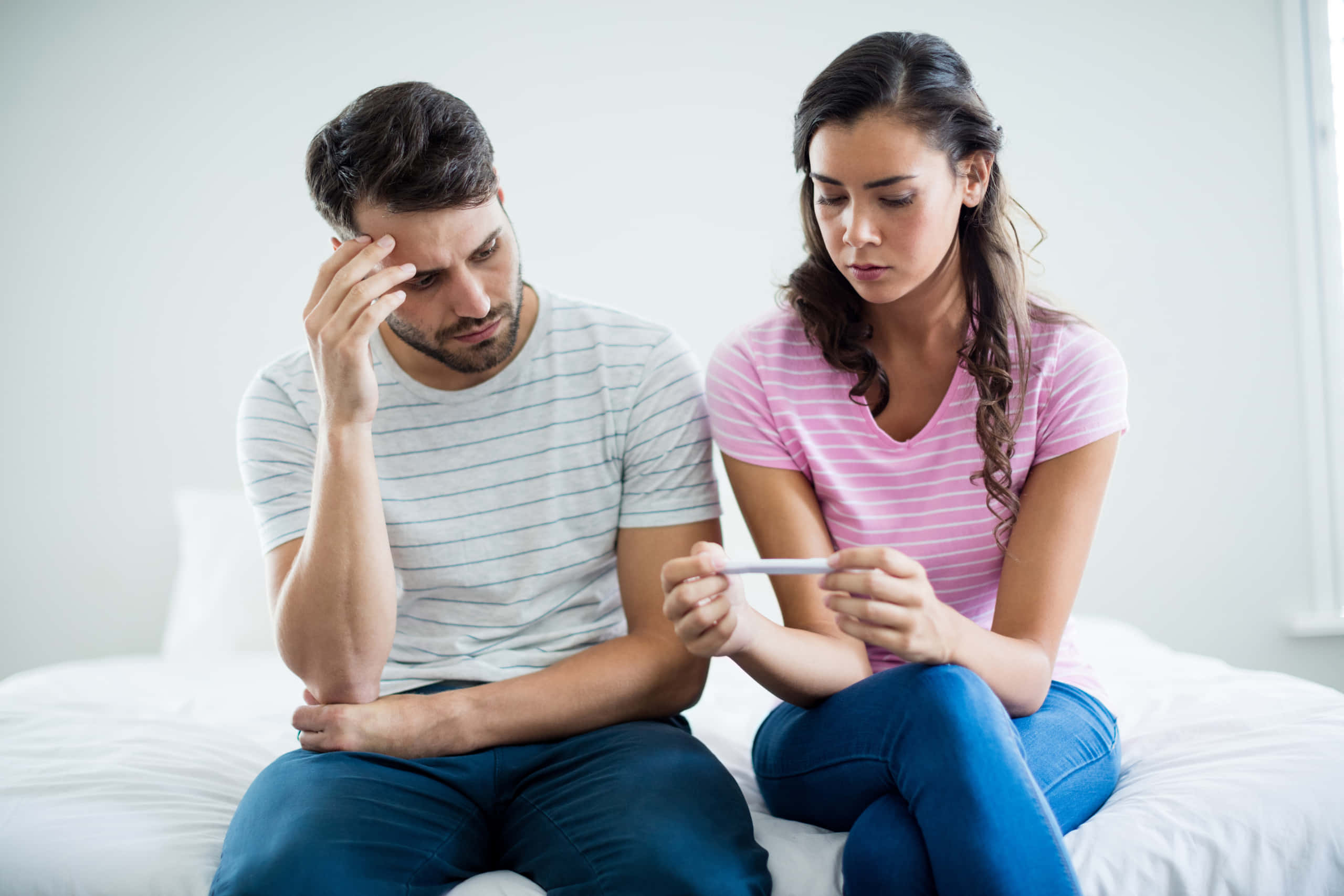 因懷孕結果而煩惱的夫婦 壁紙 — 一對情侶坐在床上，帶著憂慮的表情看著驗孕棒。