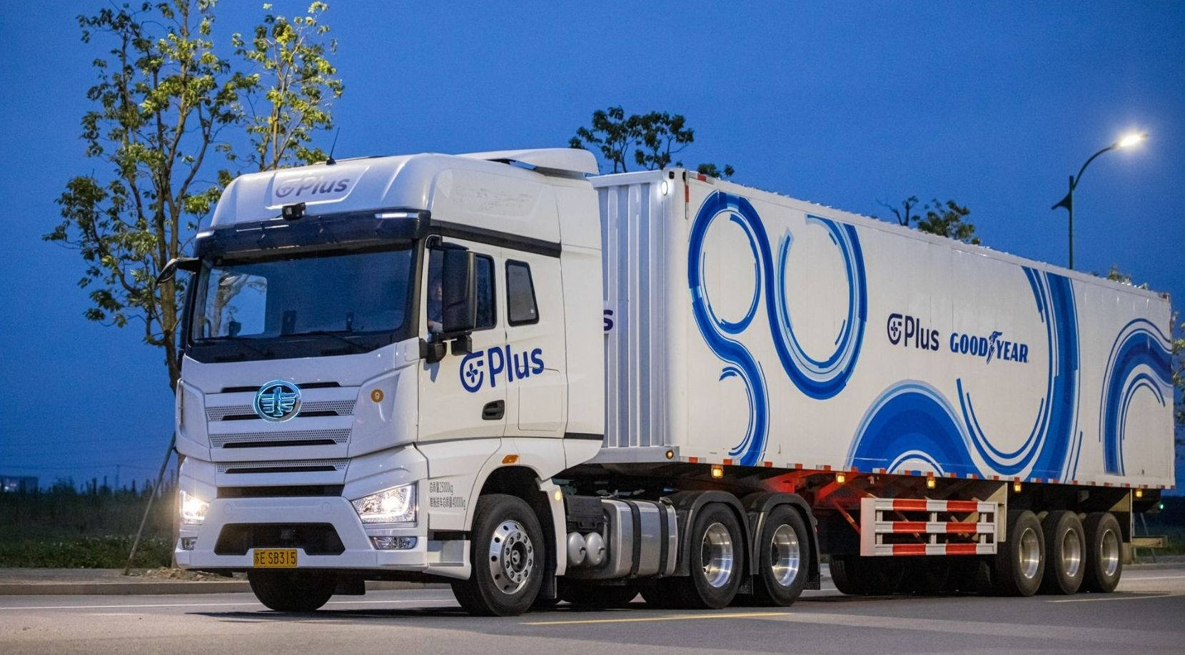 白色 Goodyear 半掛卡車，帶藍色圖案，夜間停在路燈下。