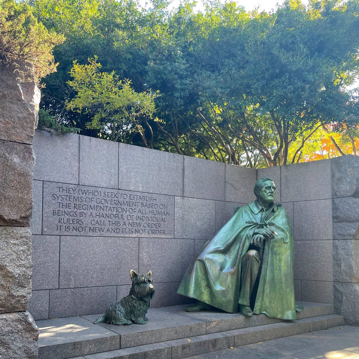 國家廣場富蘭克林·德拉諾·羅斯福紀念碑 壁紙 — 一個穿著斗篷的坐著男人的銅像，旁邊有一隻小狗，背景是刻有文字的石牆和綠樹。