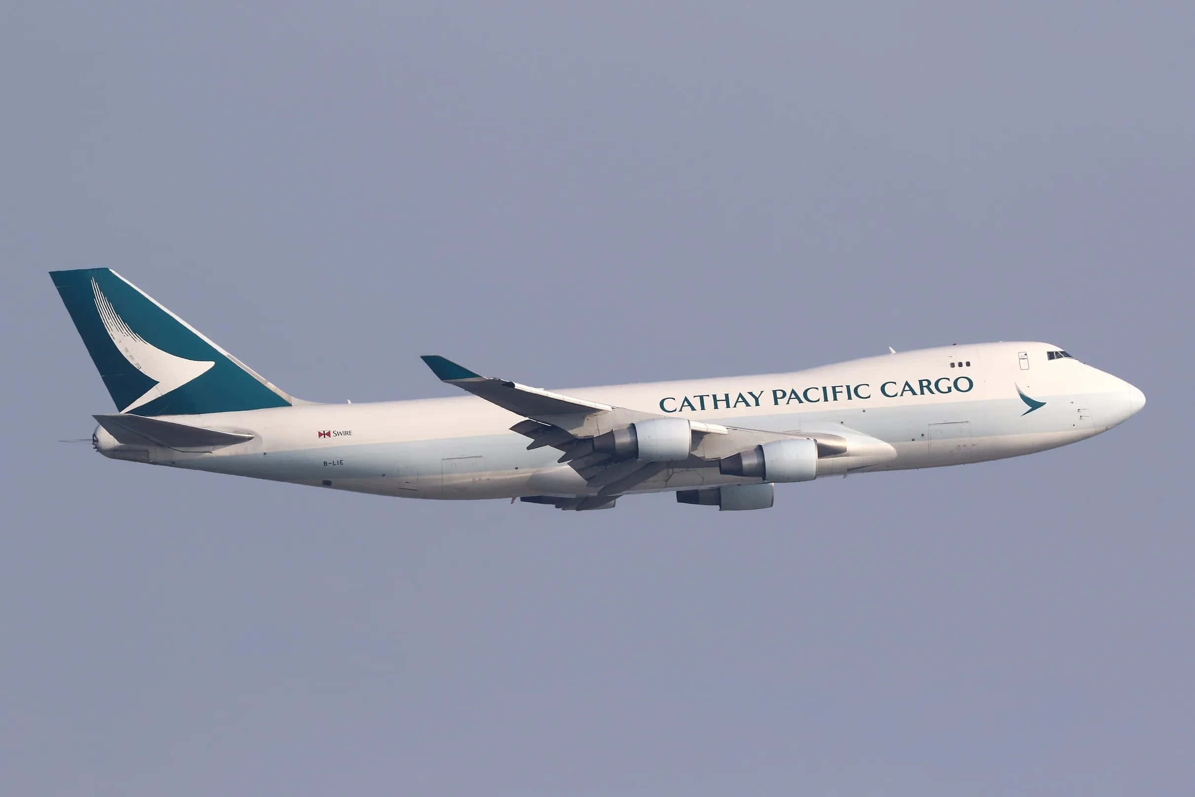 Jumbo Jets 桌布 壁紙 — 國泰航空貨運波音747在清澈淡藍的天空中翱翔，帶有獨特的青綠色和白色塗裝。