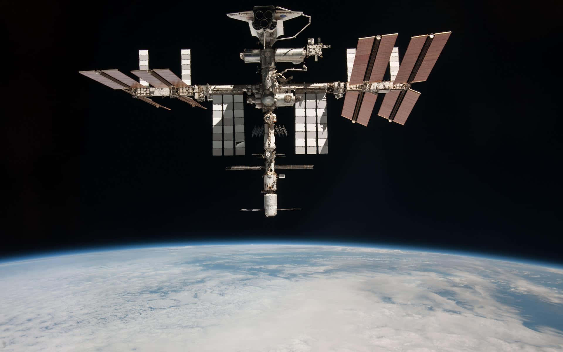 Iss 桌布 壁紙 — 國際太空站環繞地球運行，太陽能板在彎曲的藍色星球上方的黑色虛空中伸展。