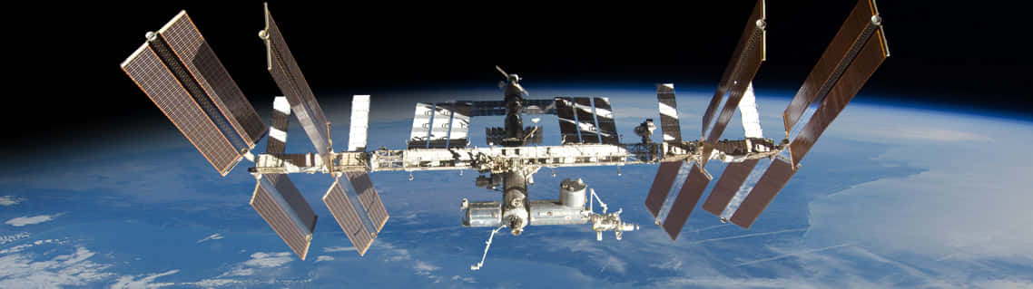 International Space Station 桌布 壁紙 — 國際太空站繞地球運行，太陽能板伸展，襯托著太空的漆黑。