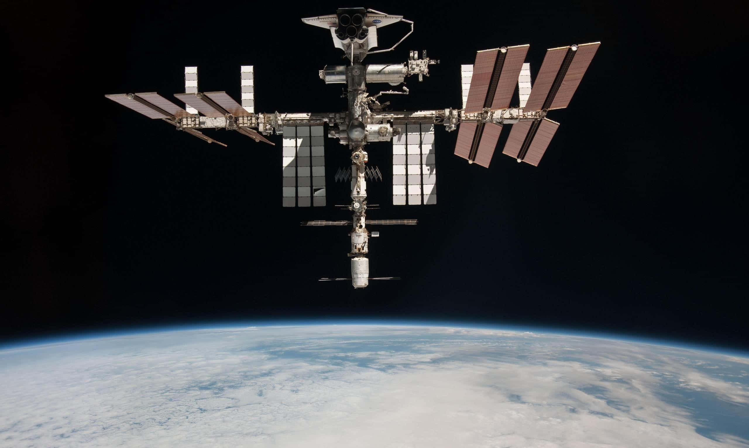Satellite 桌布 壁紙 — 國際太空站繞地球運行，太陽能板在彎曲的藍色星球上方的黑色虛空中展開。