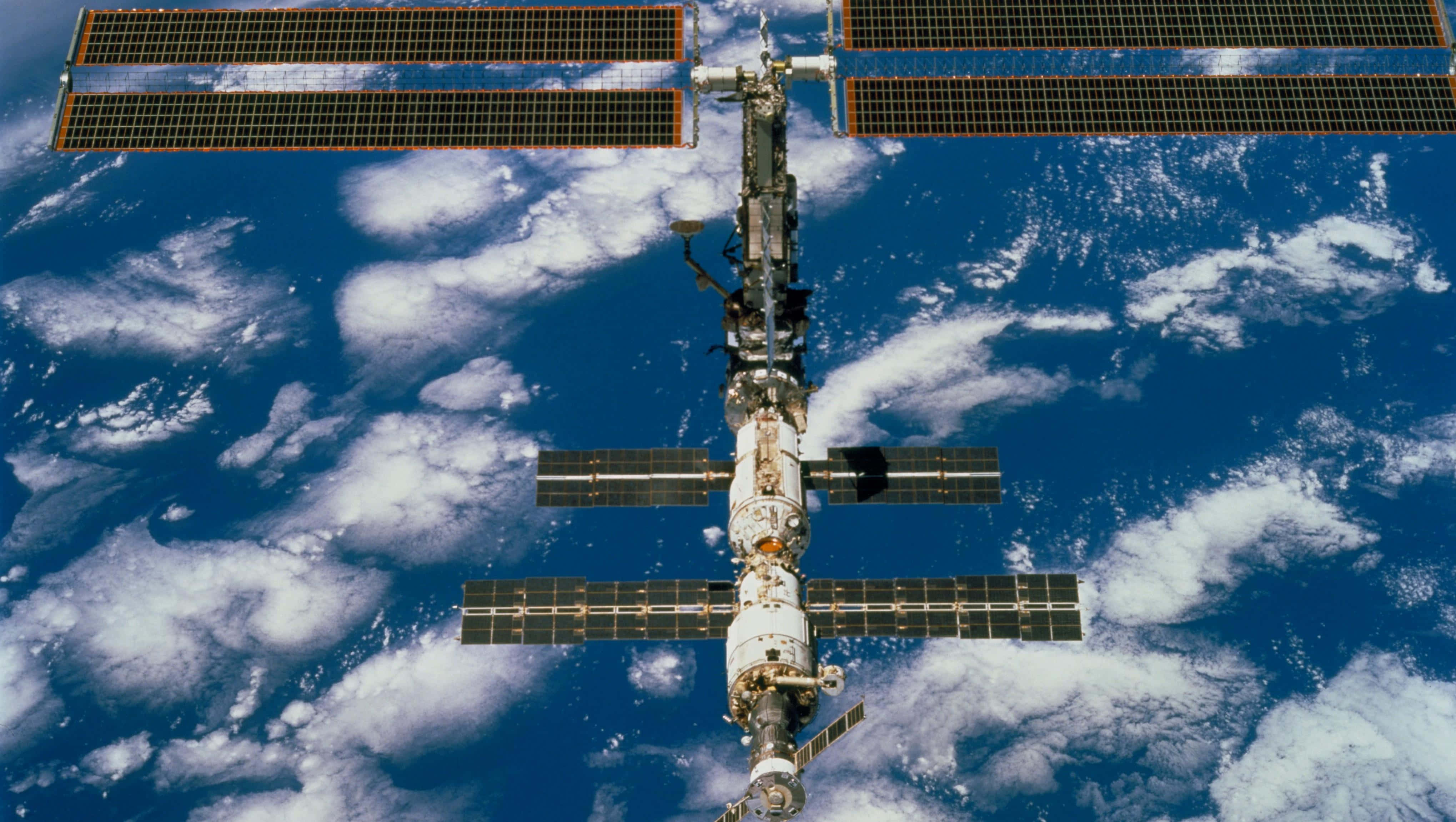 Iss 桌布 壁紙 — 國際太空站繞地球運行，太陽能板展開，背景是藍色海洋和白色雲層。