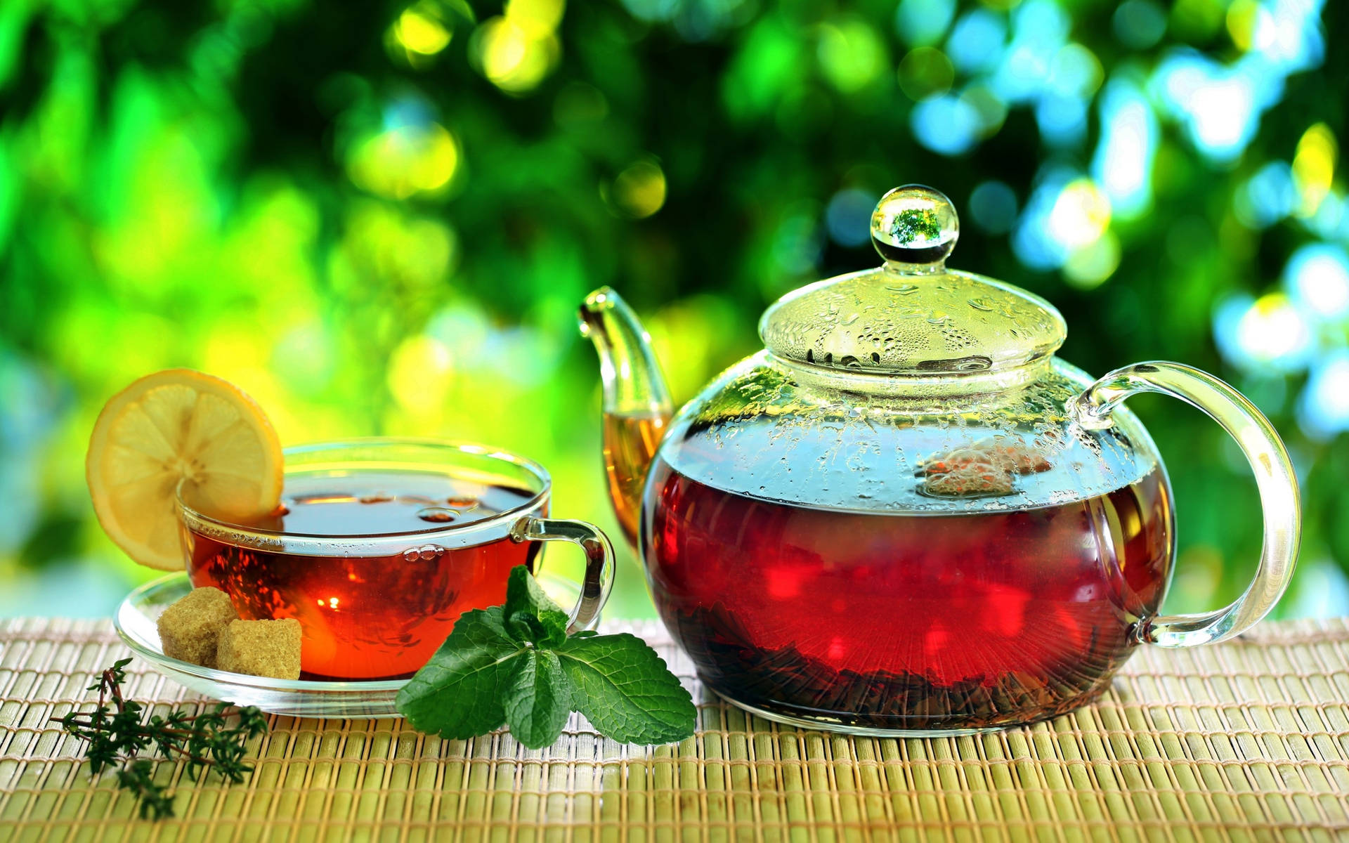 玻璃茶壺和杯子配檸檬、薄荷和糖放在竹蓆上戶外