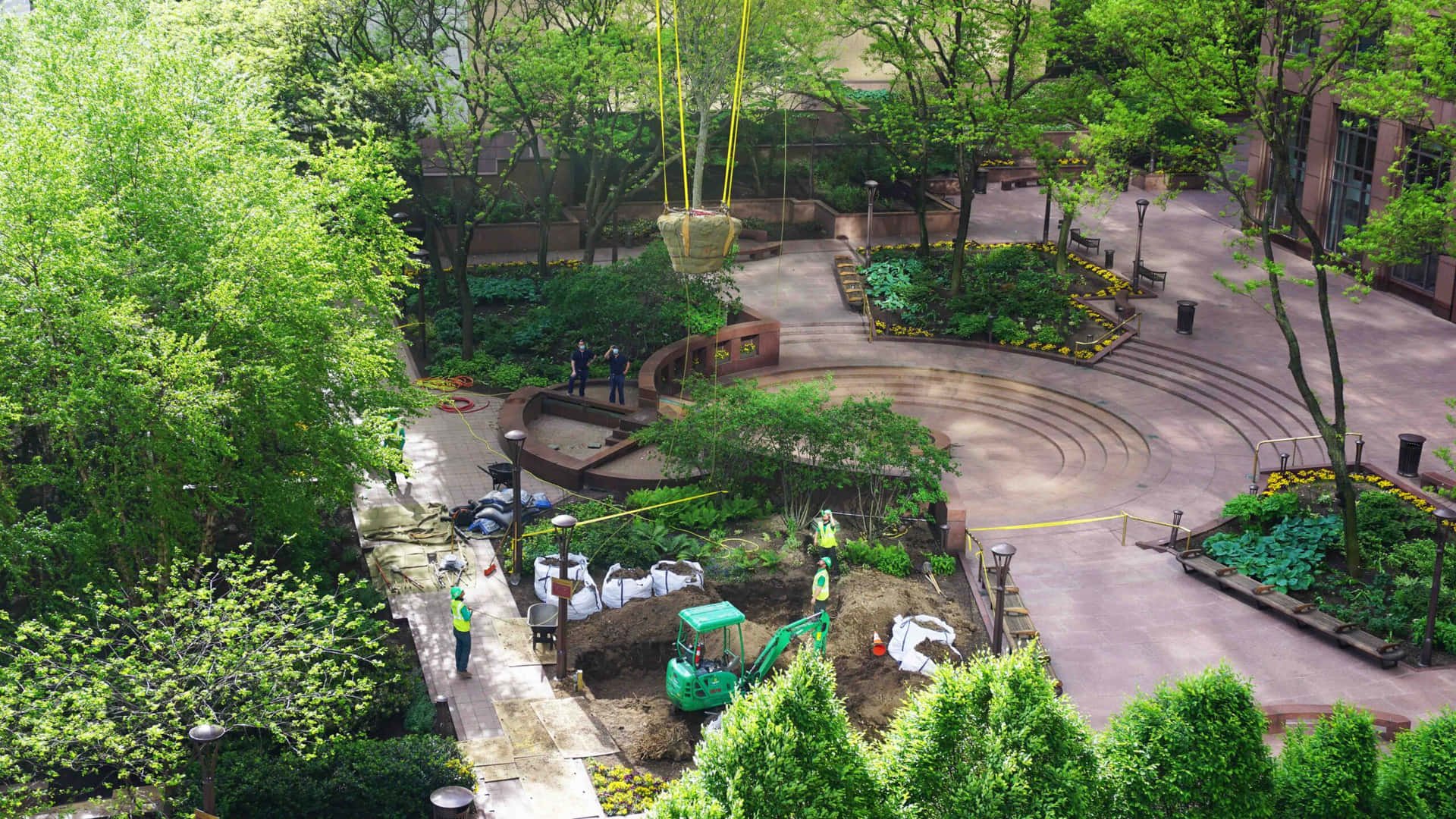 建築團隊在一個設有綠化和彎曲步道的園林城市公園中安裝一塊大石頭。