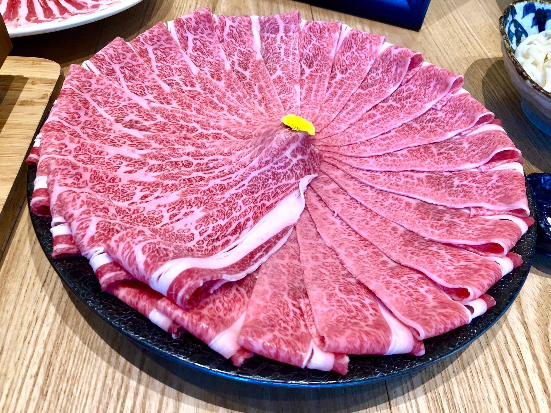 薄切雪花牛肉在黑色碟子上排列成扇形。