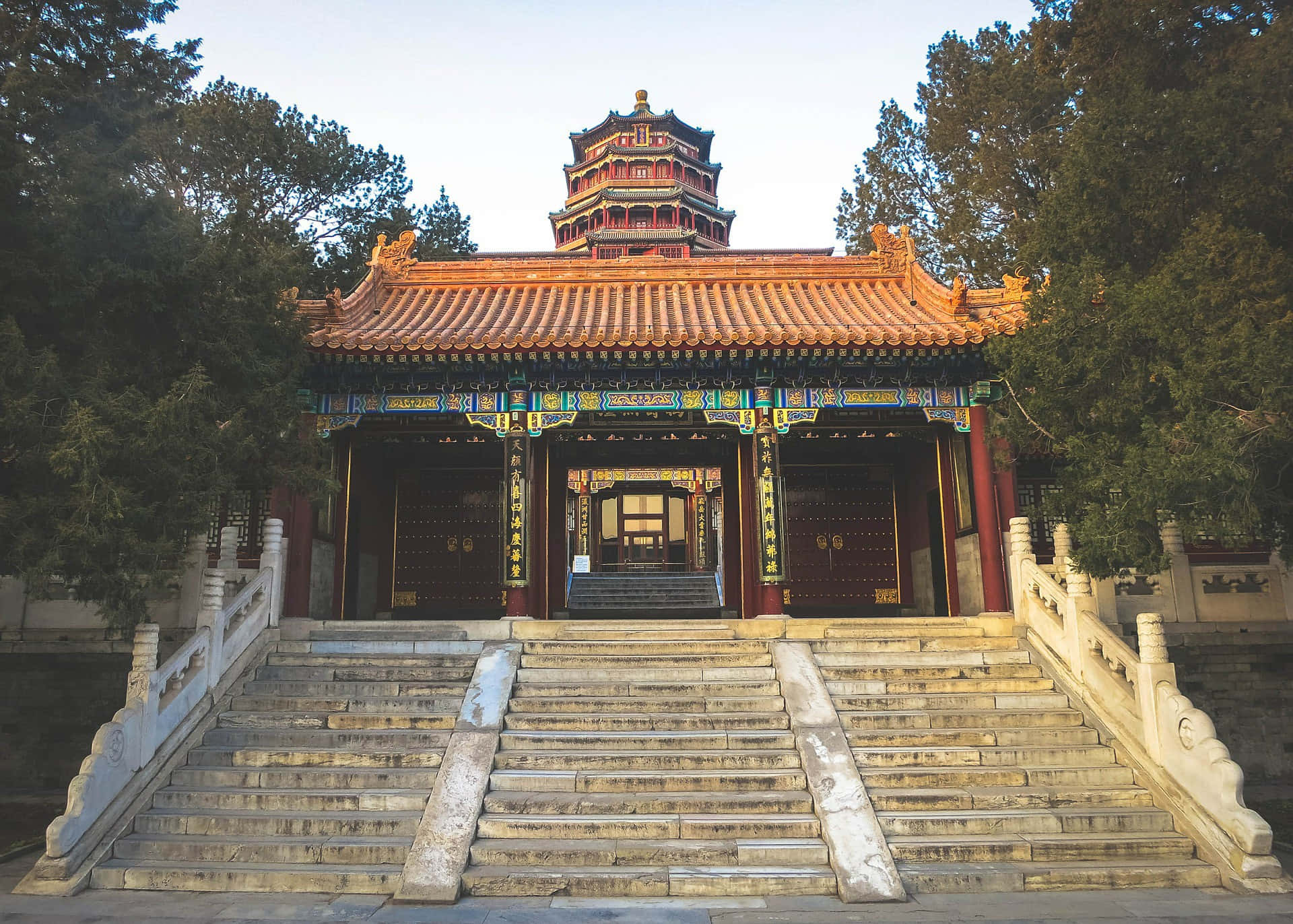 圓明園入口 壁紙 — 一座宏偉的傳統中國寺廟，擁有華麗的紅色和金色屋頂瓦片，矗立在寬闊的石階頂端，周圍環繞著高大的常青樹。