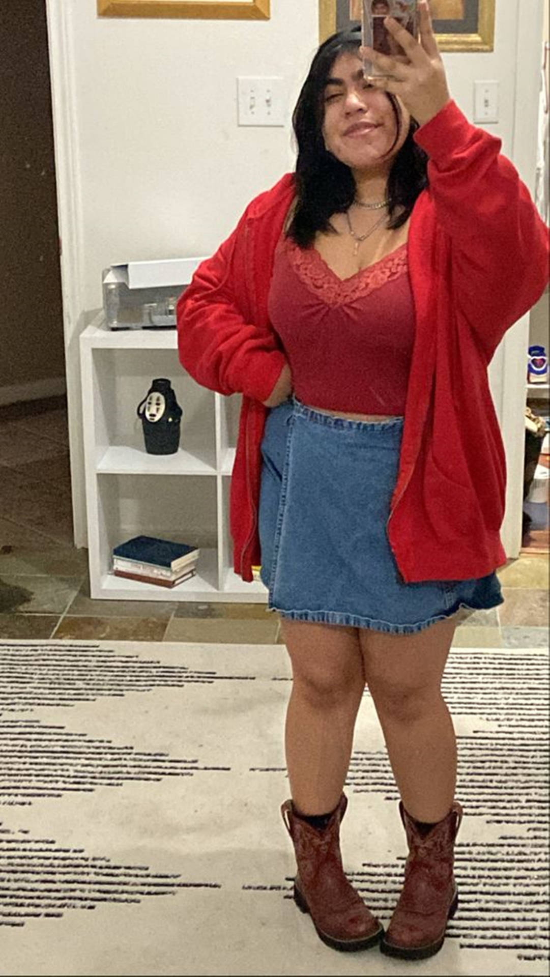 身穿紅色開襟衫和牛仔裙的女性在家中對著鏡子自拍。