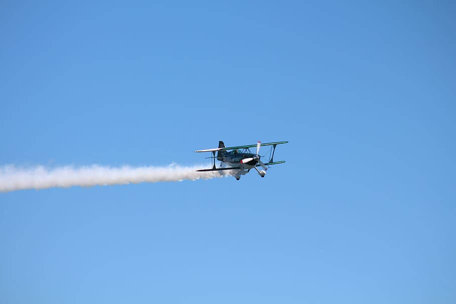 圖瓦利天空中的飛機 壁紙 — 一架復古雙翼飛機劃過晴朗的藍天，留下濃厚的白色煙霧痕跡。