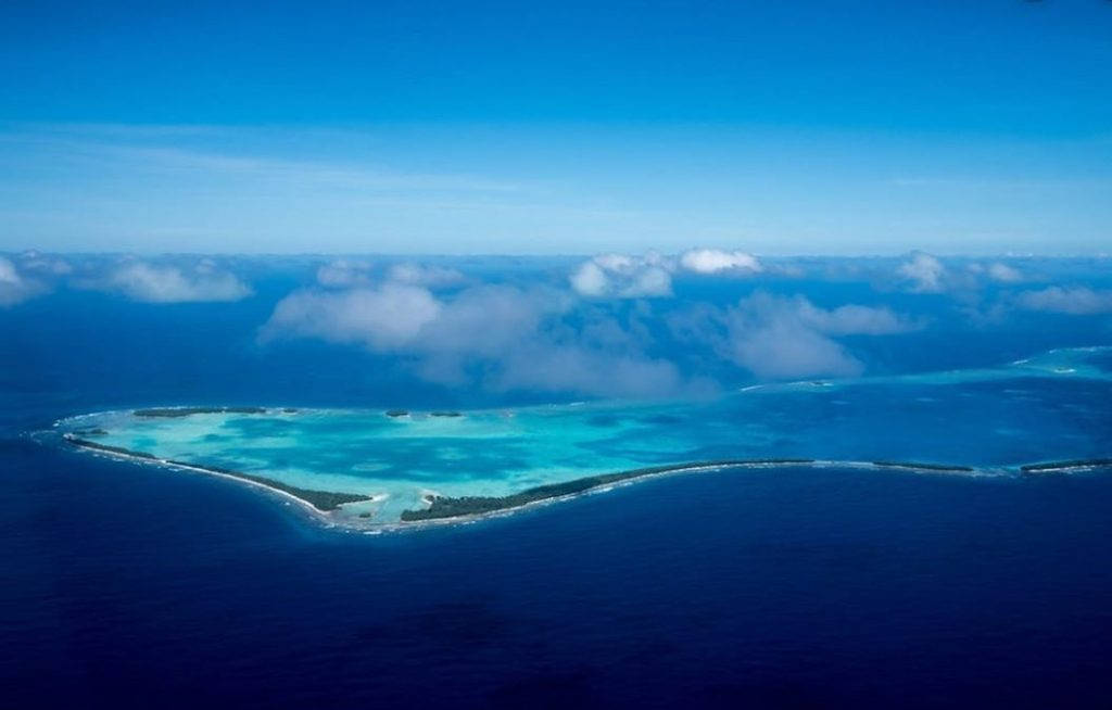 圖瓦利島空拍視角 壁紙 — 熱帶環礁的鳥瞰圖，擁有綠松石色潟湖，周圍是深藍色海洋和散落的雲朵。