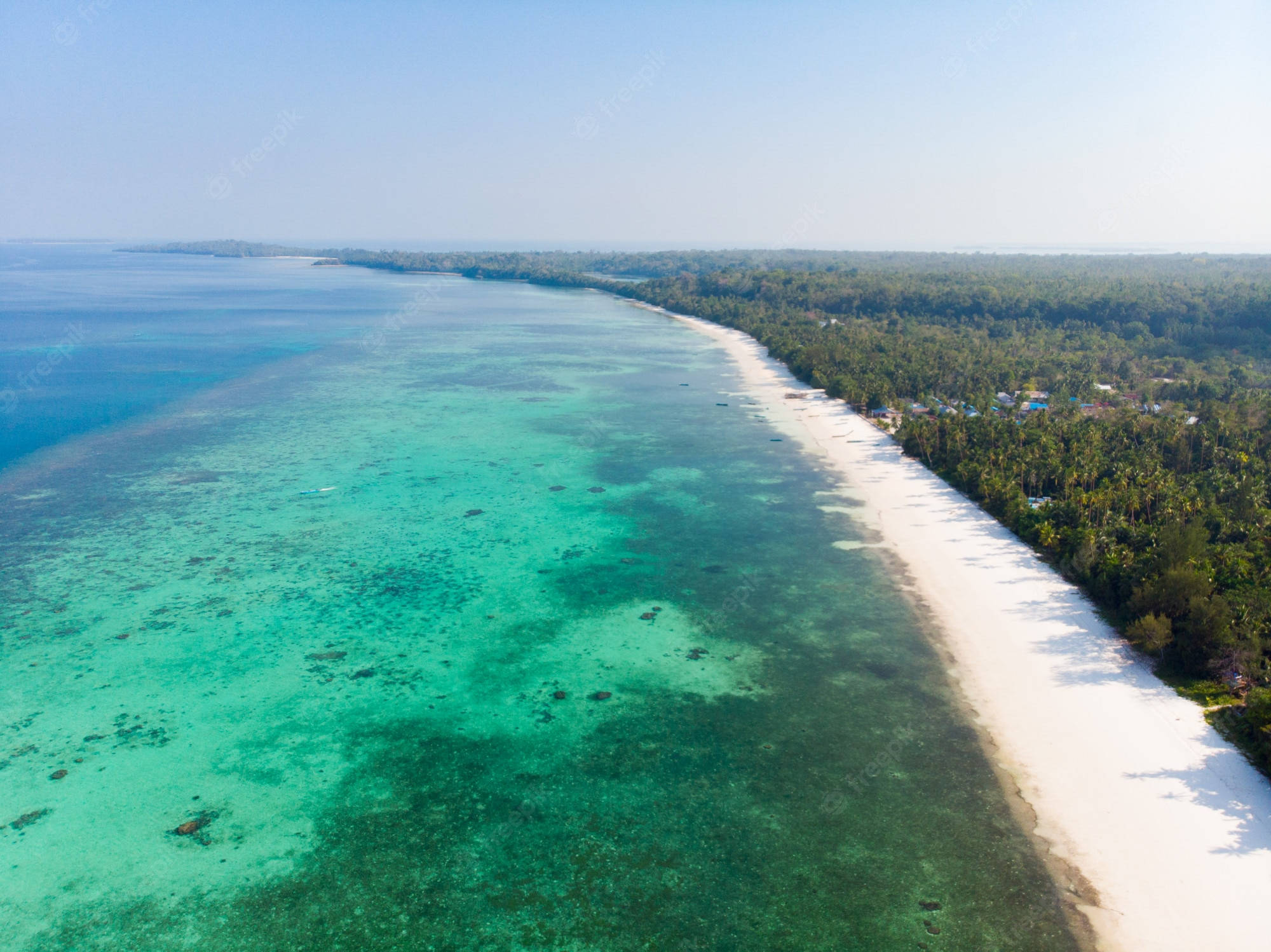圖瓦利海的翠綠海水 壁紙 — 原始熱帶海岸線的鳥瞰圖，擁有碧綠的海水、珊瑚礁和白色沙灘，周圍環繞著茂密的綠色叢林。