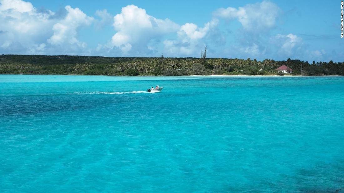 圖瓦利純淨海域 壁紙 — 一艘快艇劃過充滿活力的碧綠海水，駛向一個鬱鬱蔥蔥的綠色島嶼，天空湛藍，白雲朵朵。