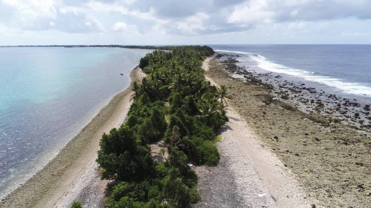 圖瓦盧島路旁樹木 壁紙 — 狹長熱帶島嶼的鳥瞰圖，島上棕櫚樹茂盛，兩側是碧綠和深藍色的海水。