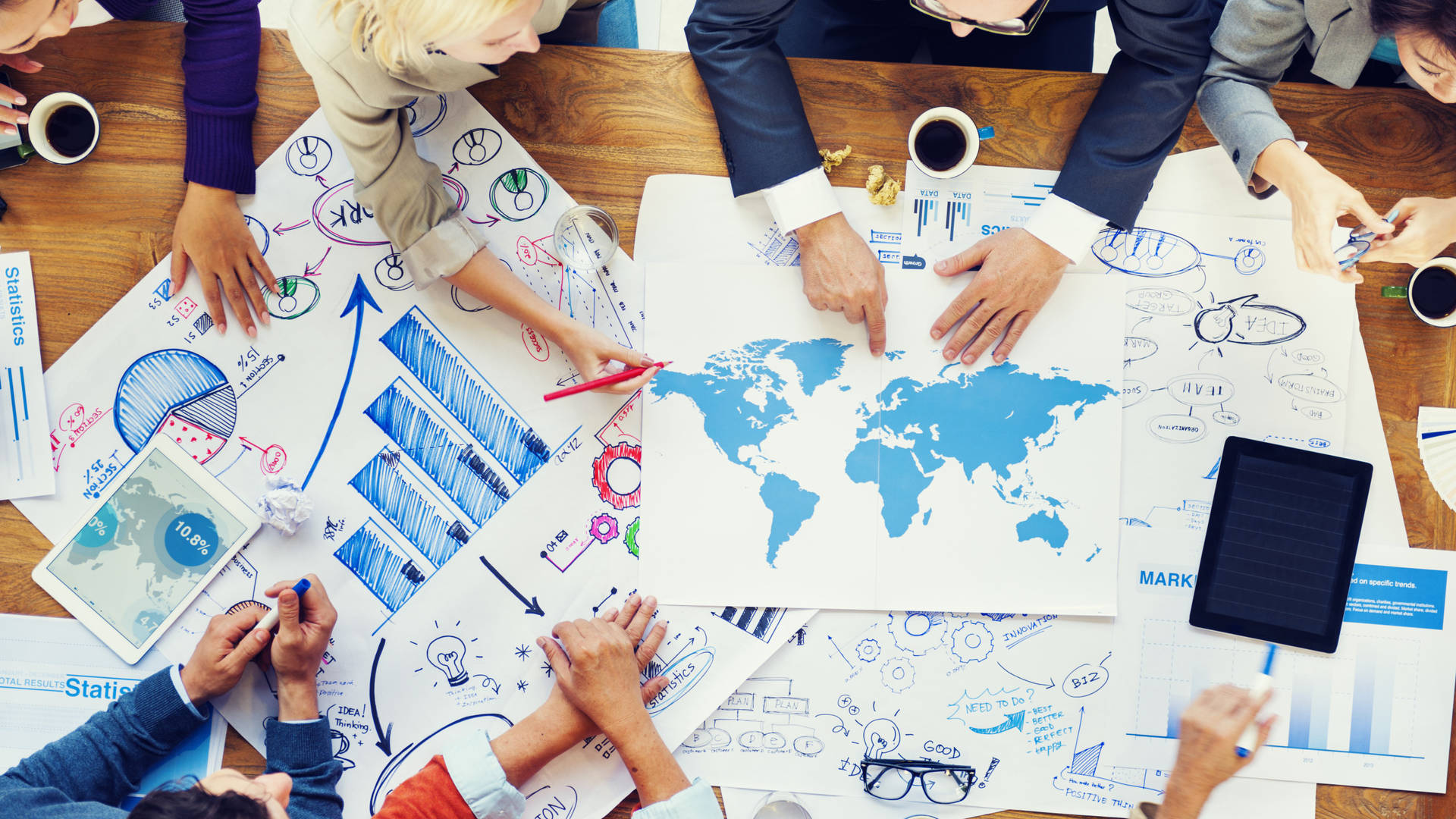Business team brainstorming global strategy with maps and charts on a wooden table.
