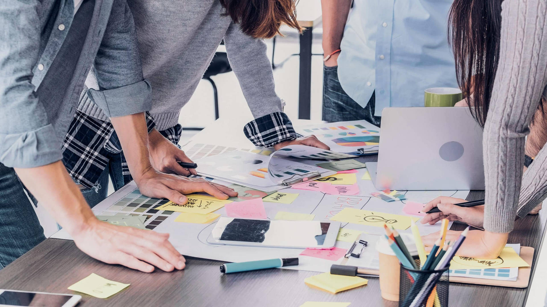 Design team brainstorming with sticky notes and laptops on a wooden desk.