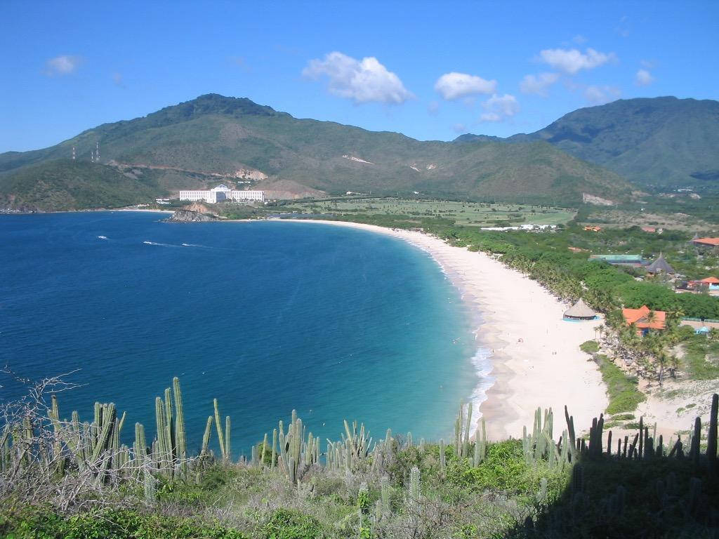 土克島與開曼群島山景 壁紙 — 在明亮的藍天下，綠色的山脈和仙人掌環繞著一個碧綠的海灣和白色沙灘的廣闊景色。