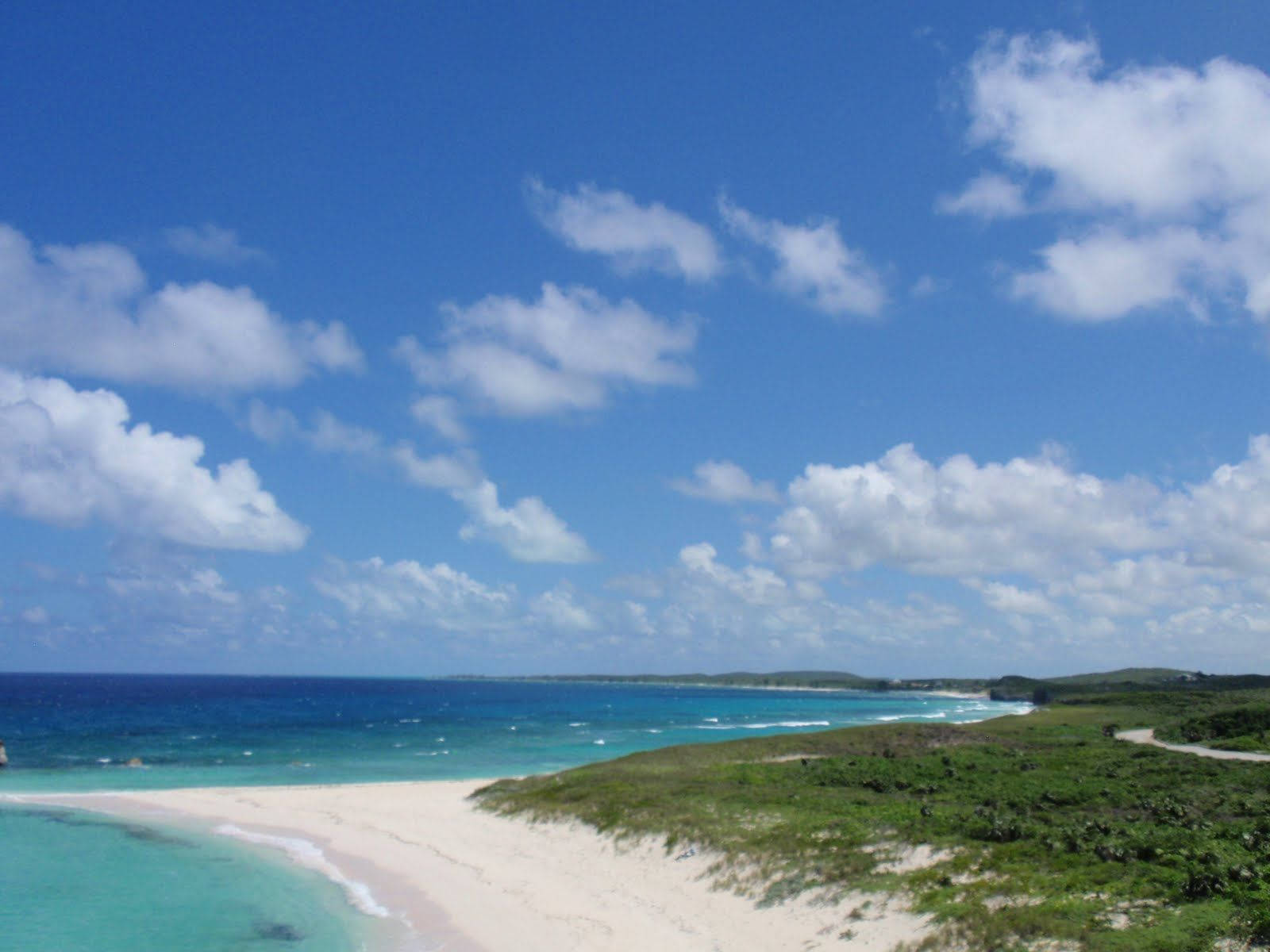 土克島與開曼群島海濱風光 壁紙 — 一個寧靜的熱帶海灘，擁有碧綠的海水、溫柔的海浪、白色的沙灘和蓬鬆的雲朵，在明亮的藍天下。